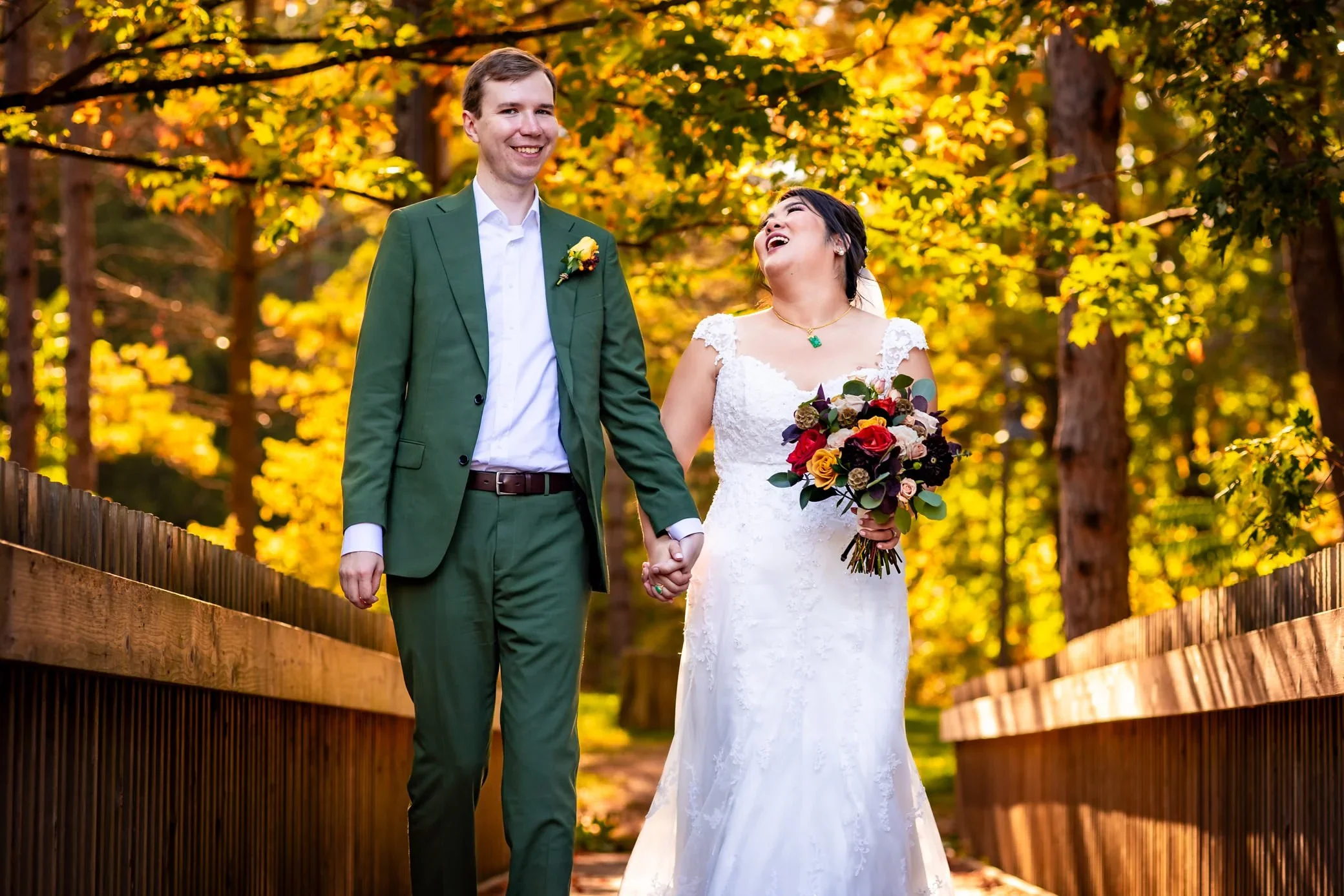 Bride and groom walking hand in hand through fall colours at McMichael Canadian Art Collection during their outdoor wedding portraits near Toronto.