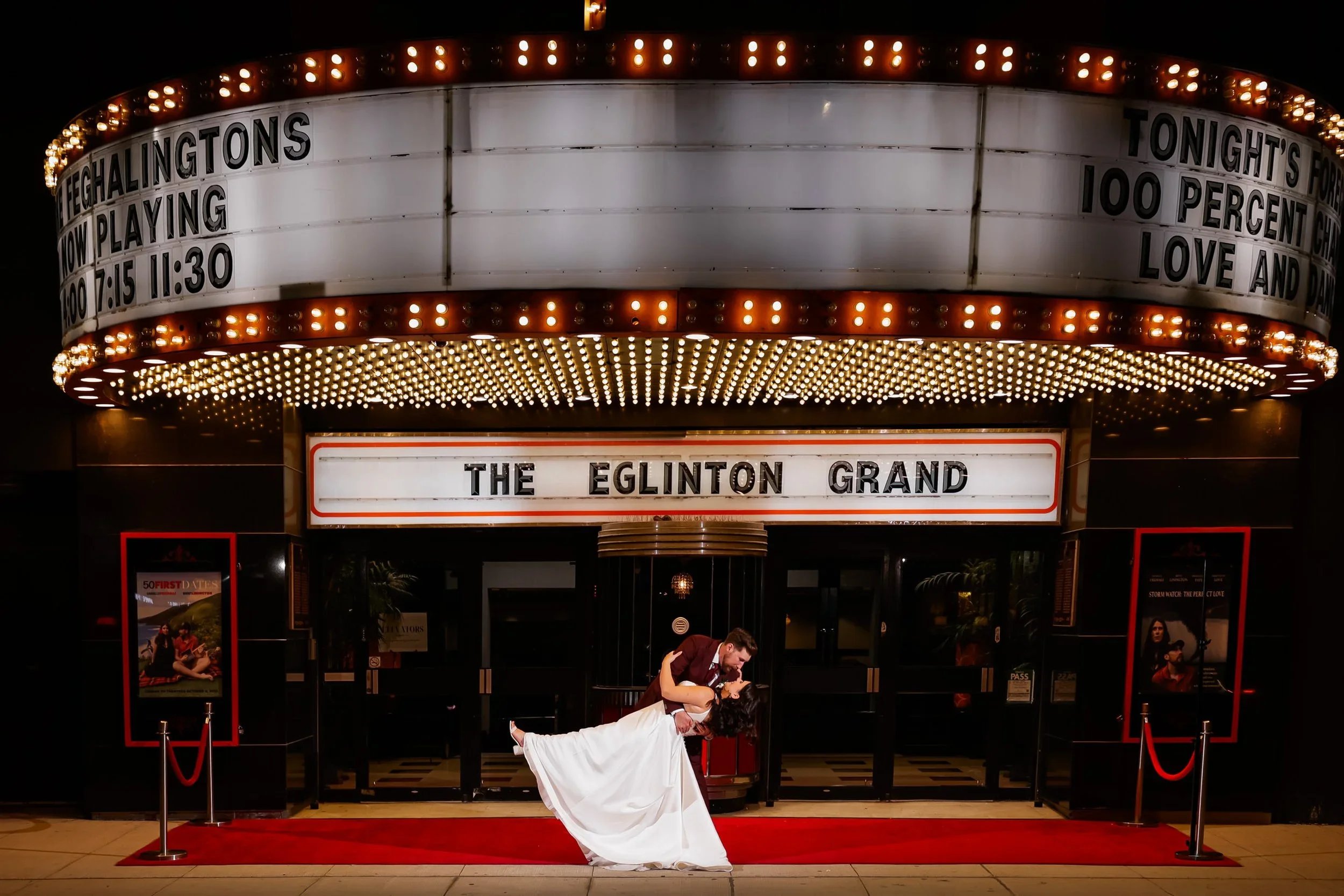 Night wedding portrait outside The Eglinton Grand in Toronto with the couple dipping under the illuminated theatre marquee