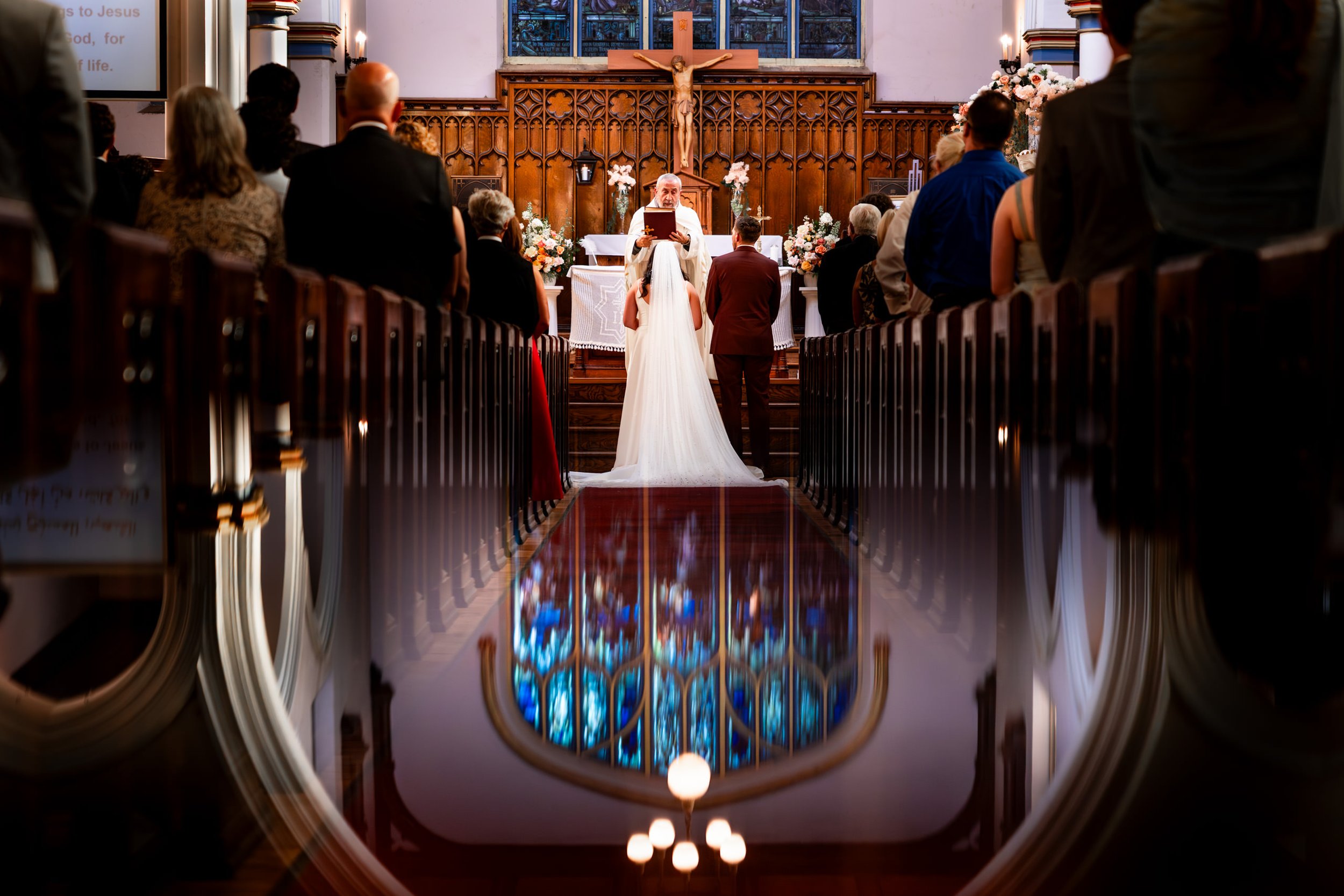 bride and groom standing at altar during wedding ceremony in Toronto church with dramatic reflection on polished aisle floor