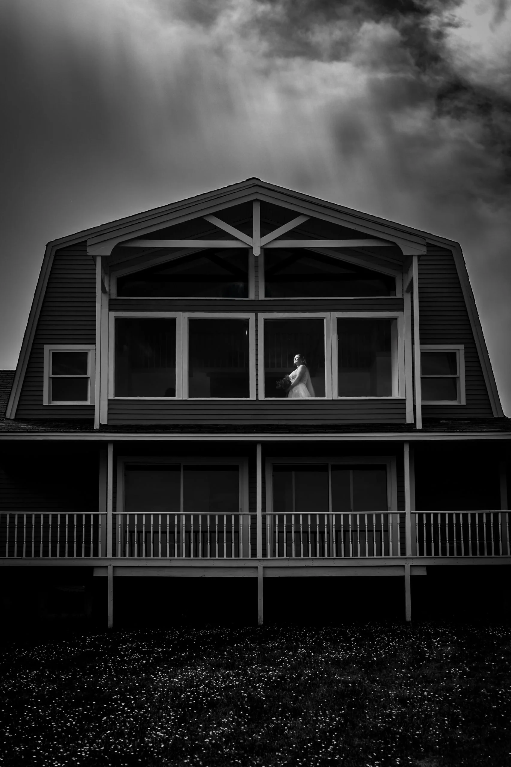 Moody black and white photo of a bride looking out the top-floor window at Clinton Hills during her PEI wedding.