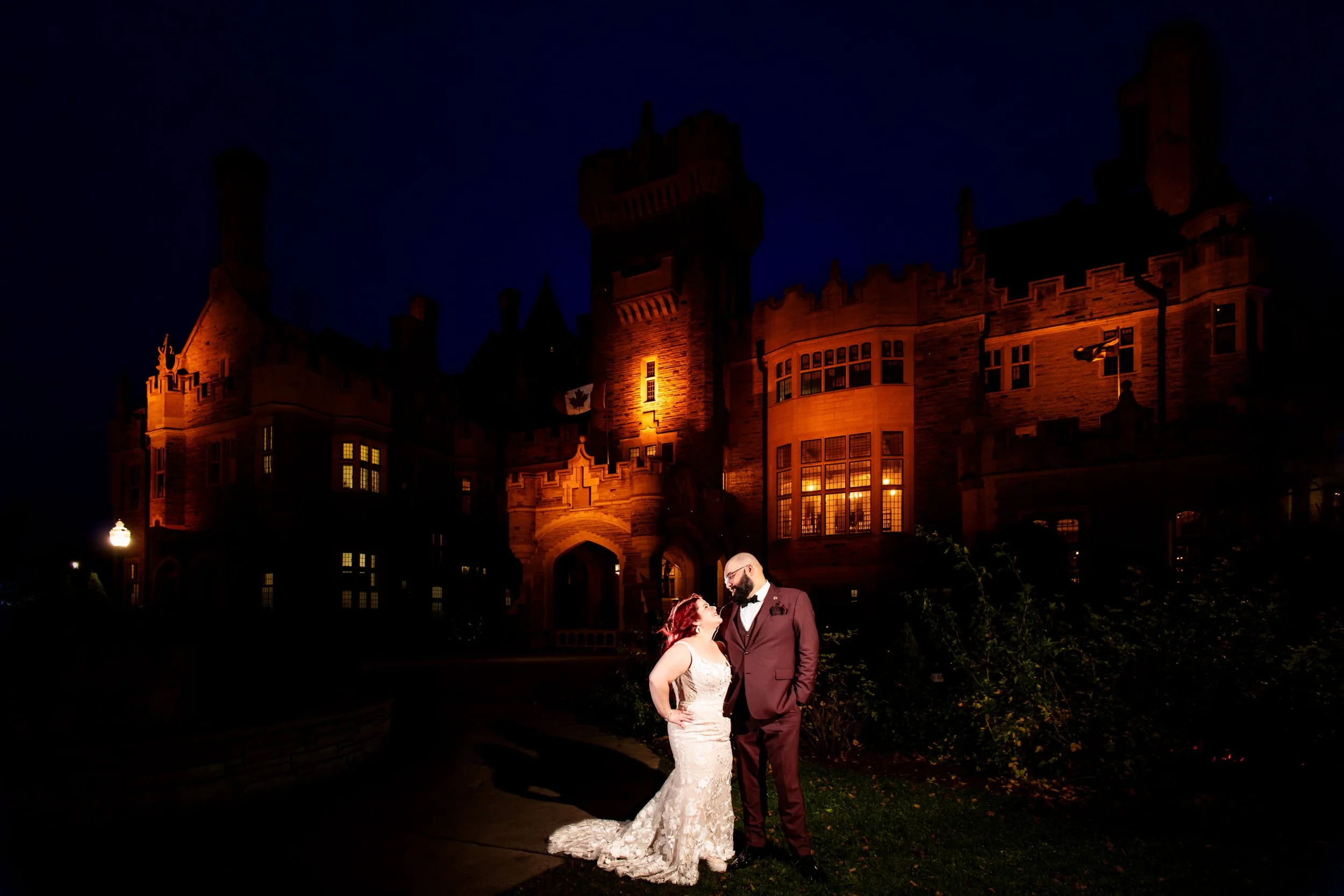 Bride and groom posing in front of Casa Loma at night during a Toronto wedding, with the castle glowing behind them