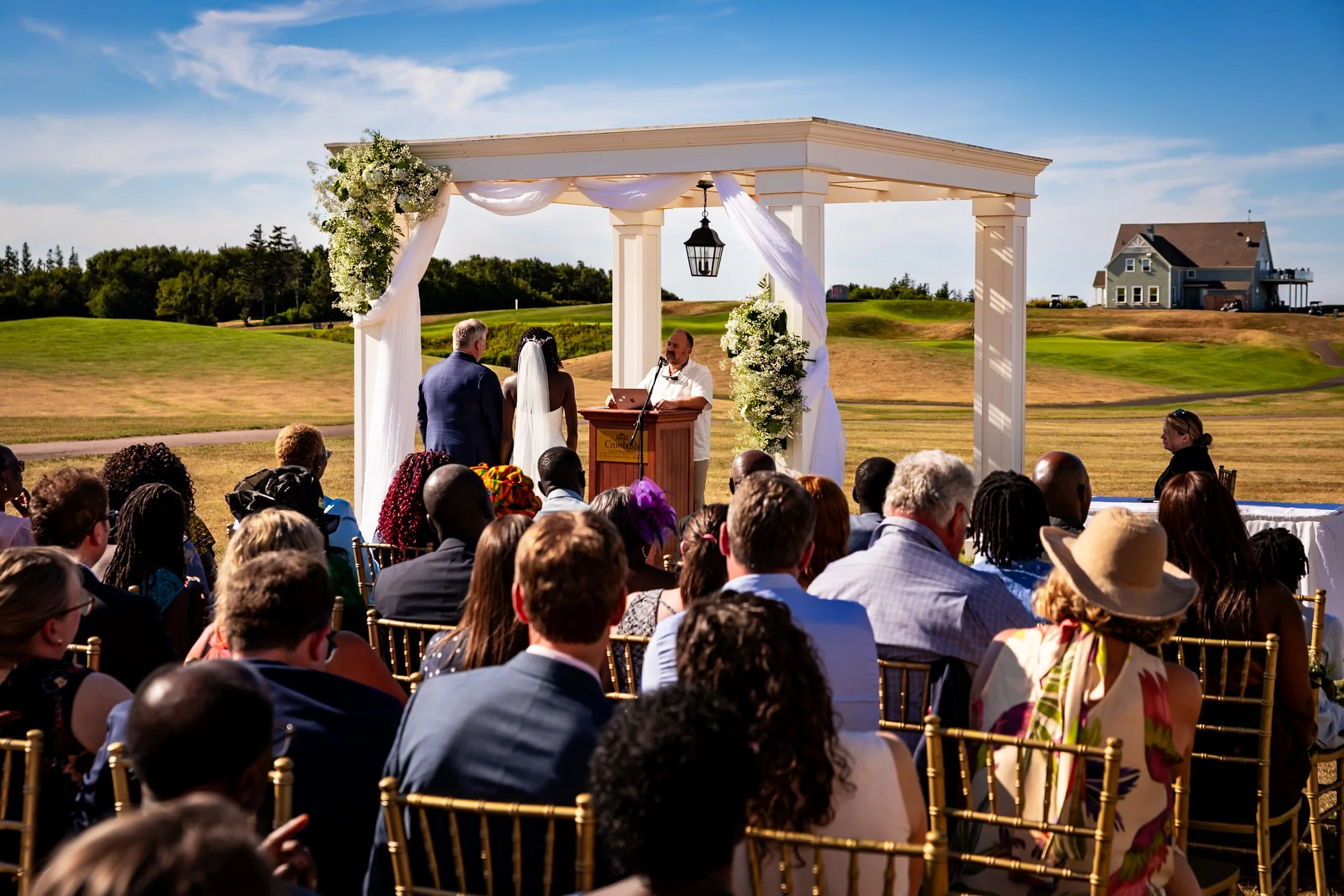 Outdoor wedding ceremony at Rodd Crowbush Golf & Beach Resort in PEI, with Anita and Alex standing under a white floral arch in front of their guests.
