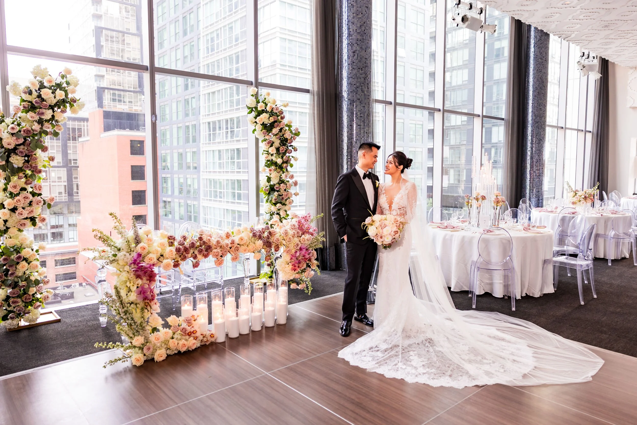 Terri and Jeremy posing in front of a floral ceremony arch at Malaparte in downtown Toronto, with floor to ceiling windows, city skyline views, and modern wedding reception decor inside TIFF Lightbox