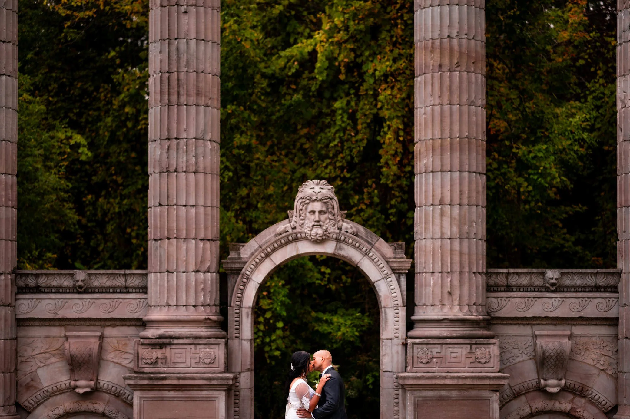 Bride and groom kissing in front of the historic columns at The Guild Inn Estate in Scarborough