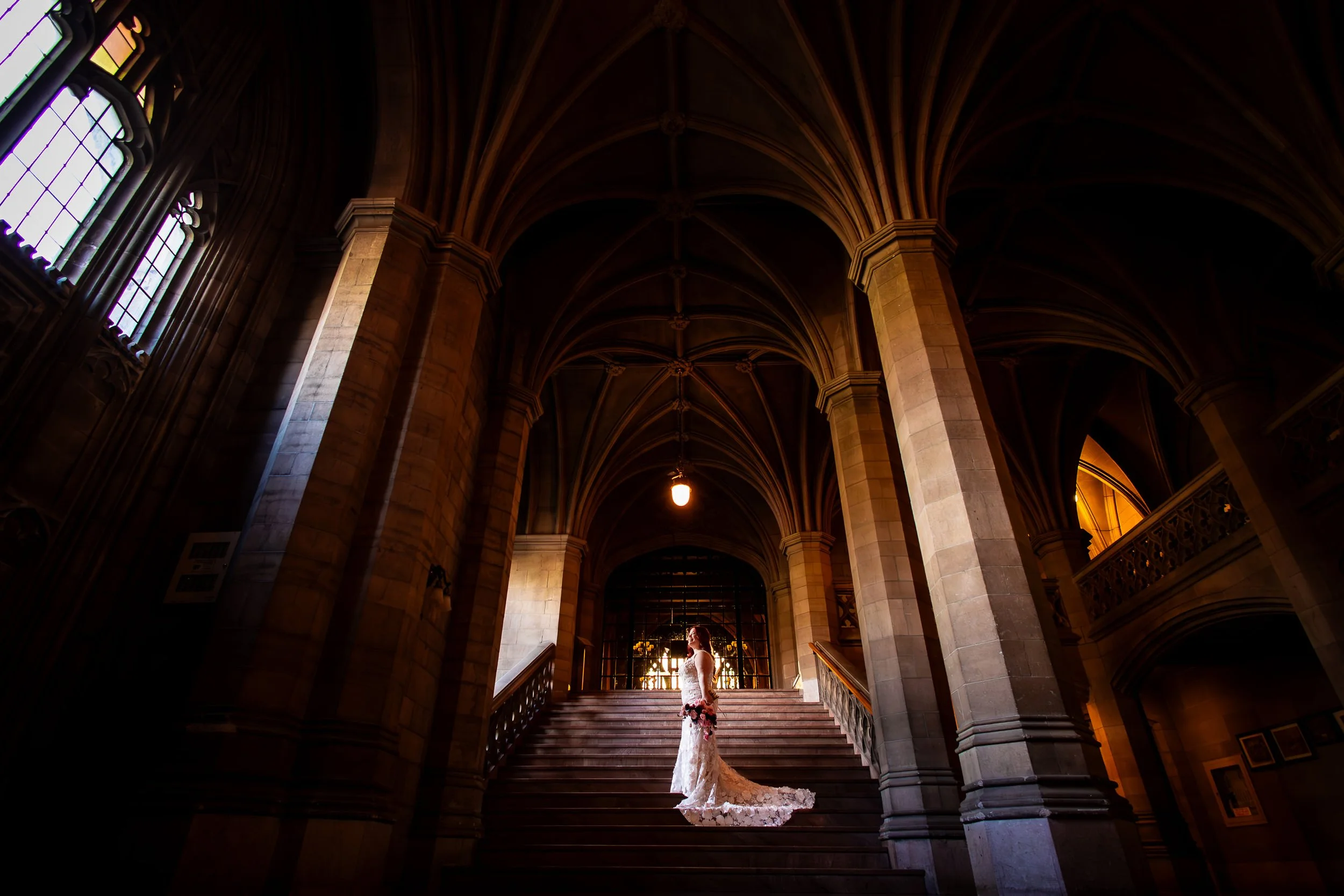 Bride standing on a grand stone staircase with dramatic arches and warm light, elegant Toronto wedding portrait