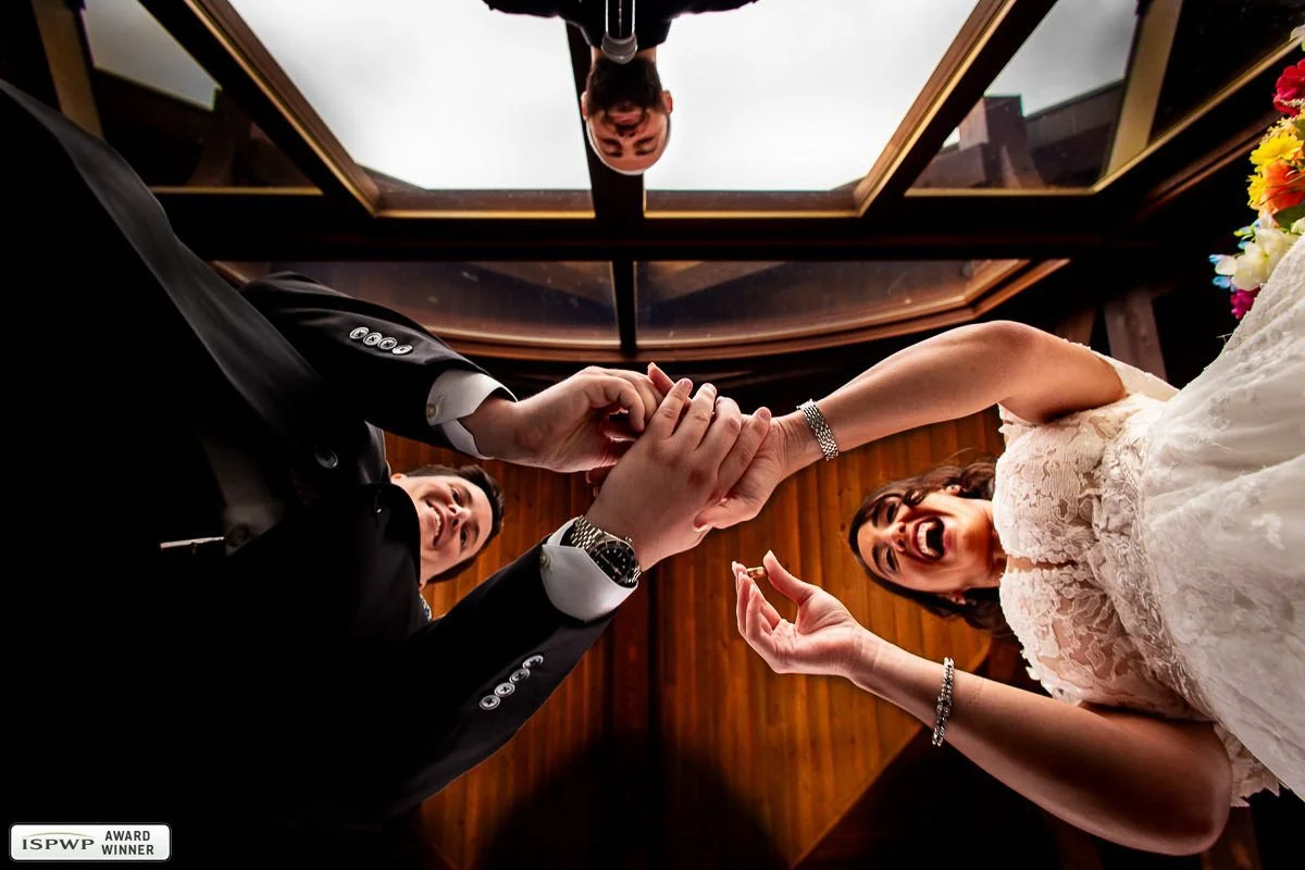 Creative low angle photo of a bride and groom exchanging rings beneath a skylight during their wedding ceremony