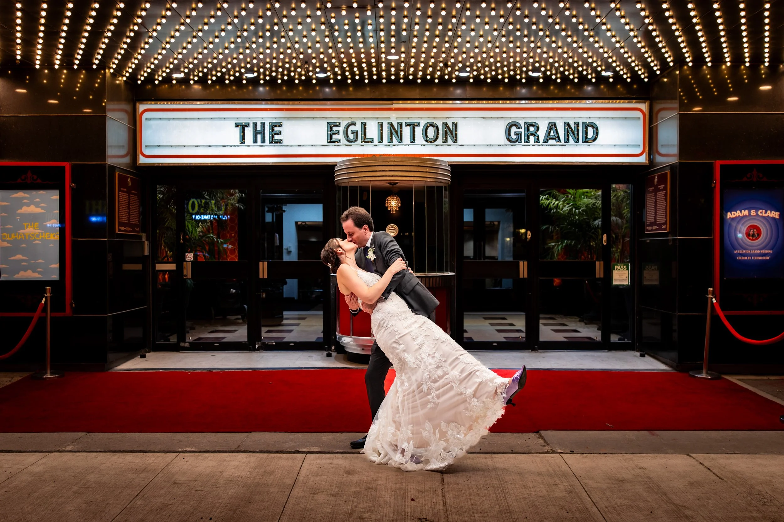 Couple kissing in front of The Eglinton Grand marquee in Toronto with red carpet and theatre lights