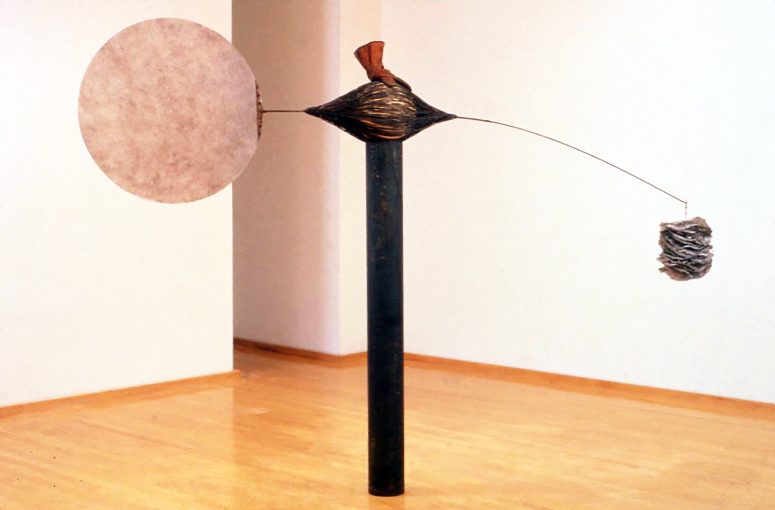  In The Balance II, 1993, 80 x 120 x 11 inches   One of the strongest sculptures in this recent show, In The Balance II, measures a stack of ruffled wire-mesh disks against a large, upright fiberglass plate whose shape and position suggest a gong, ex
