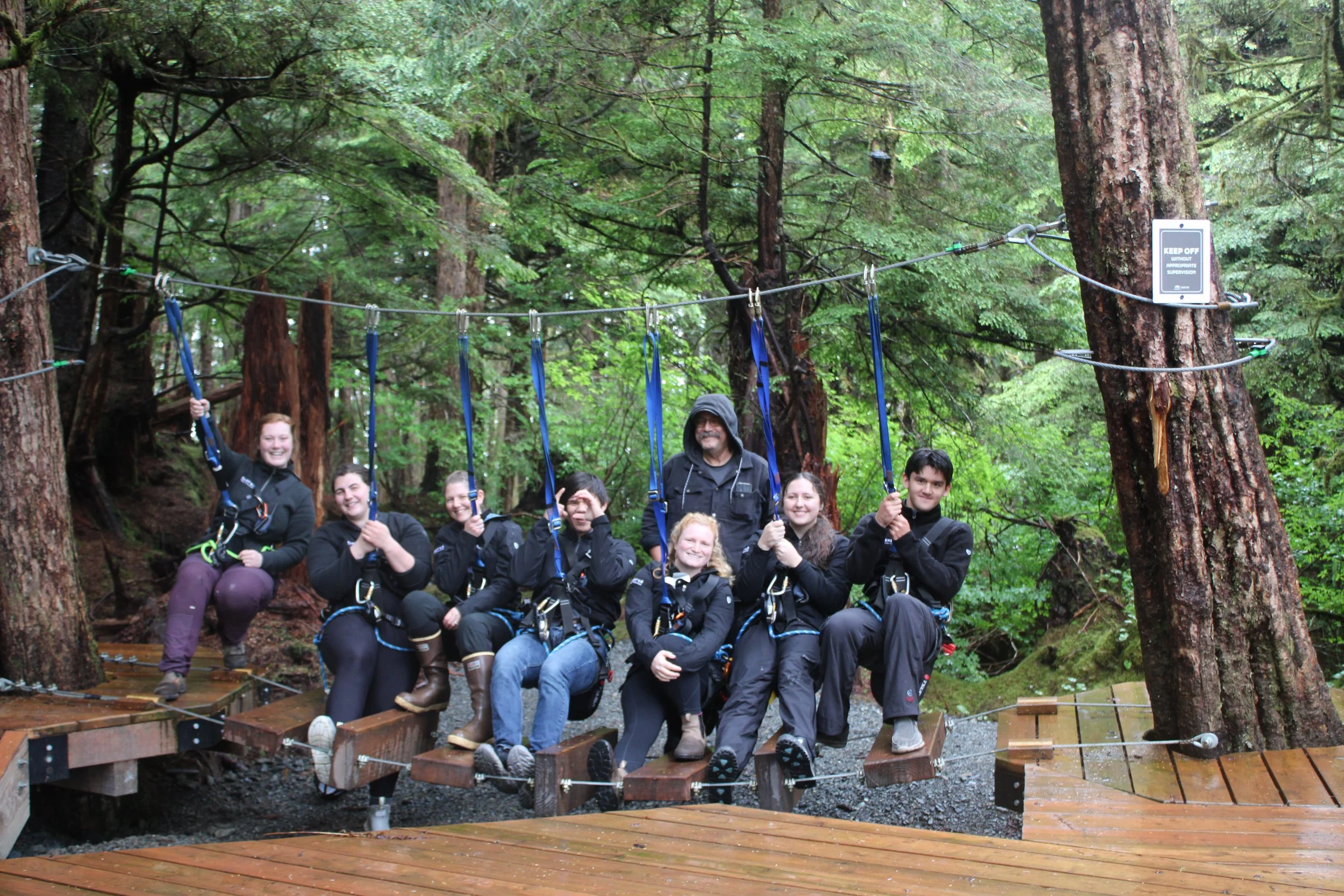 group of 8 aerial course staff sitting in safety gear on course