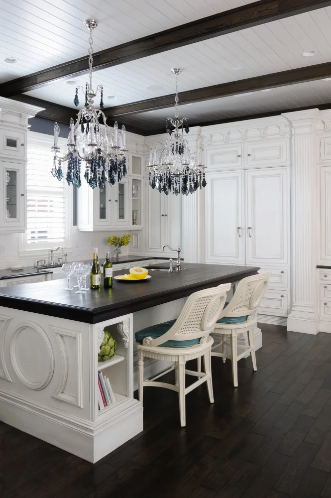 This luxury white kitchen creates drama by contrasting with darker materials, such as the Wenge wood countertop, dark beams, and hardwood floors.