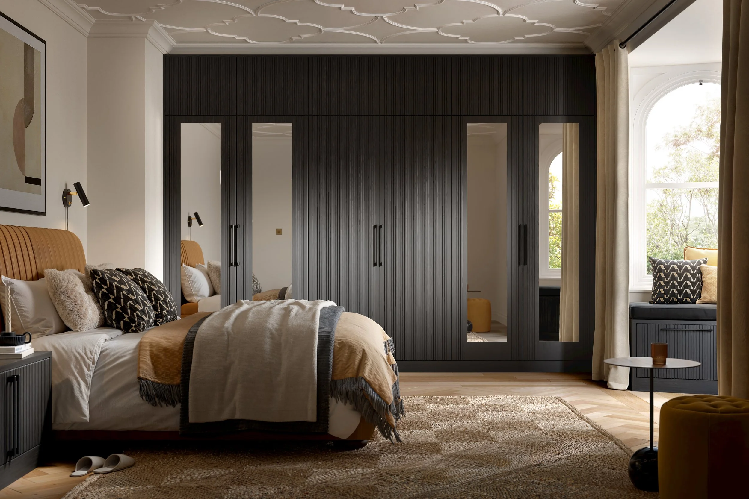 Elegant bedroom featuring a black floor-to-ceiling mirrored wardrobe, tan upholstered bed with layered neutral bedding, herringbone wood flooring, and an arched window seat with mustard accents.