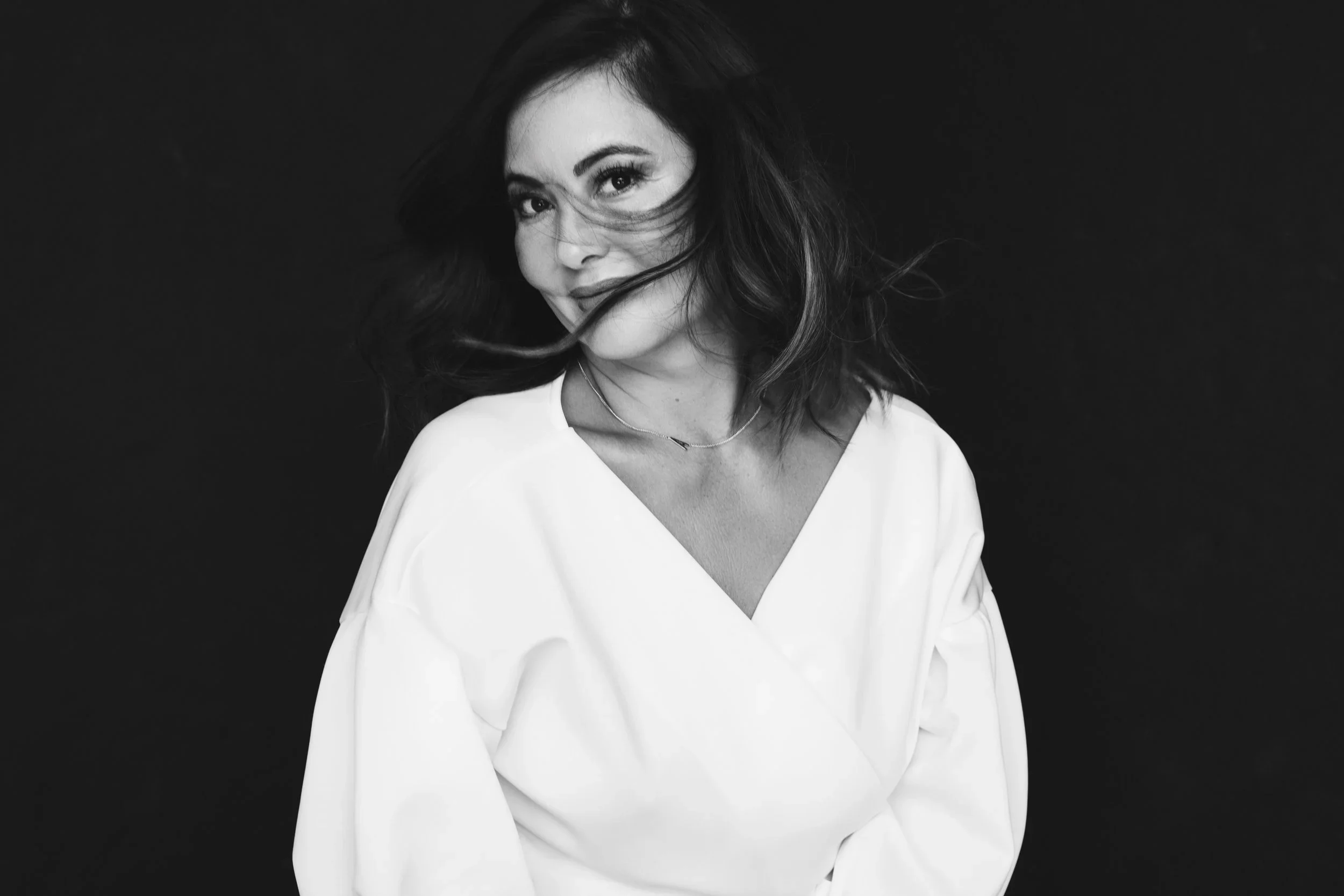 A monochrome portrait of a woman with windswept hair and a gentle smile, creating a playful yet intimate mood.