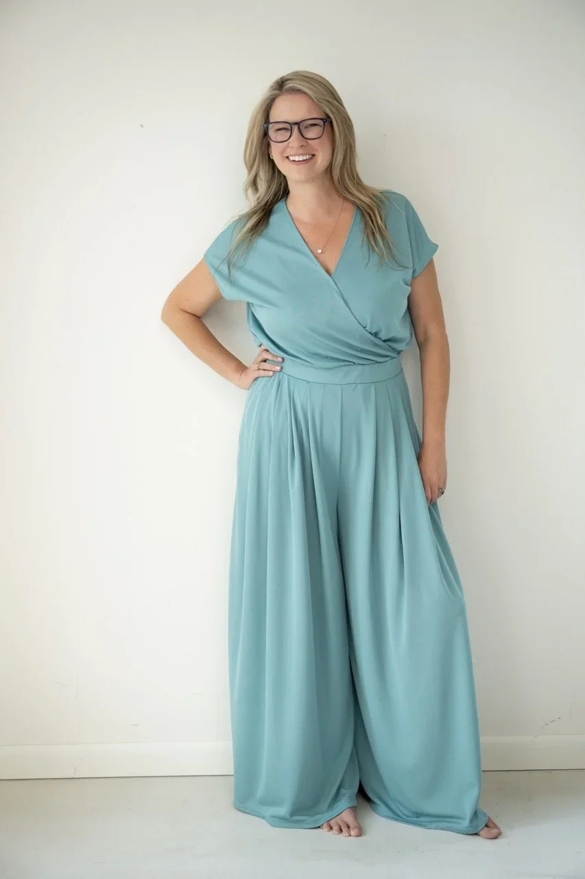 A full-length portrait of a woman standing with ease and self-assurance. Soft posture, open stance, and an effortless smile that feels genuine not posed. The clean backdrop and flowing silhouette keep the focus on her presence: confident, relaxed, an