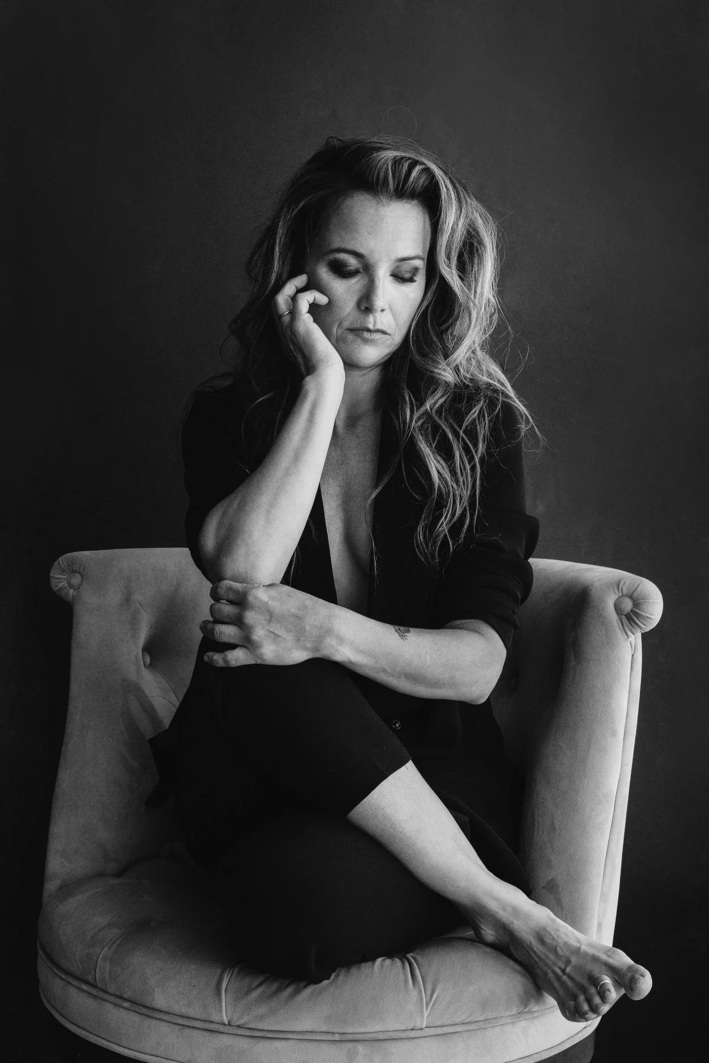 A black-and-white portrait capturing stillness and self-trust. Seated with ease, her posture is relaxed yet intentional—grounded, reflective, and fully at home in her presence. This image speaks to a woman who no longer rushes to be seen, because she