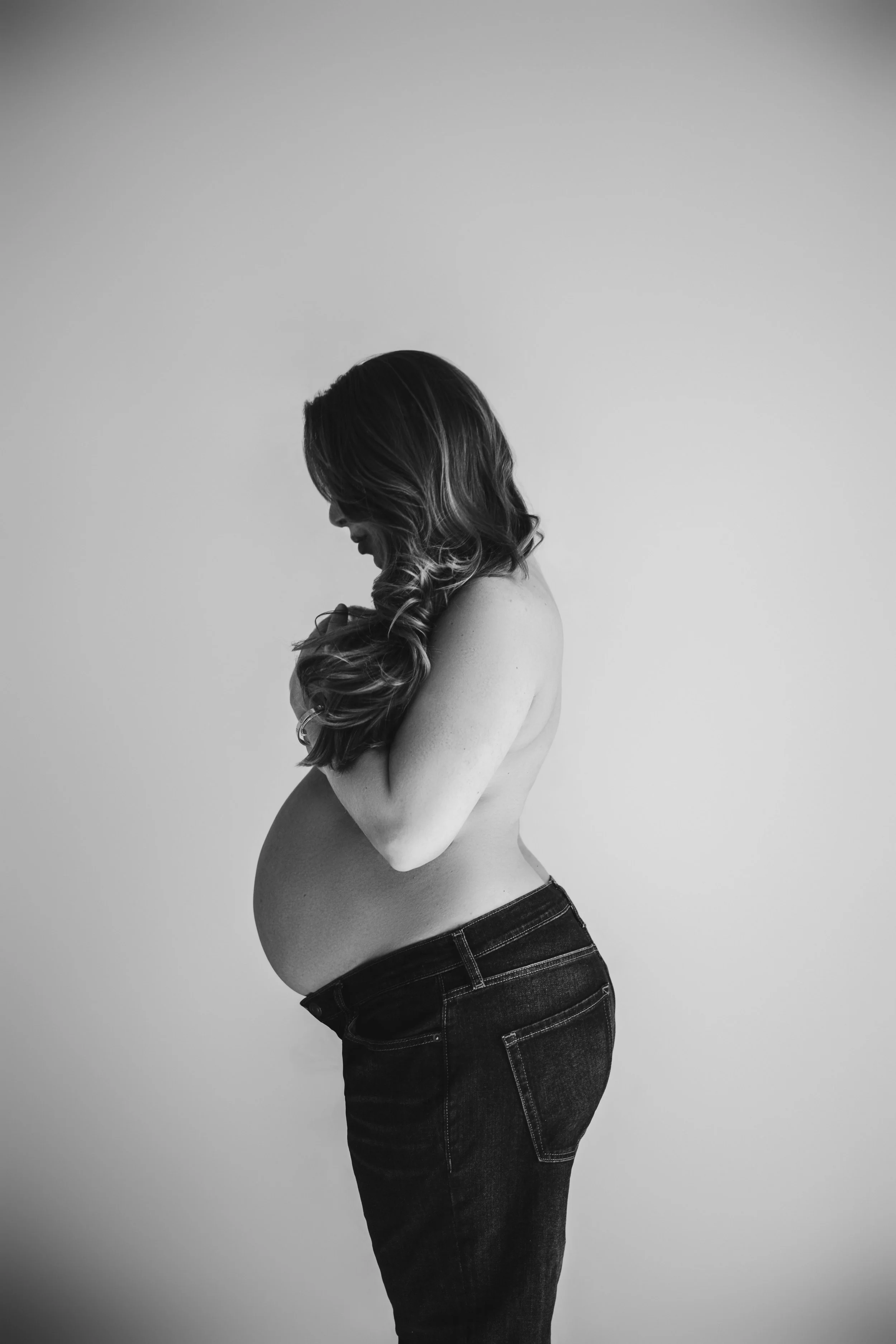 Elegant black and white maternity portrait of pregnant woman holding baby bump in studio