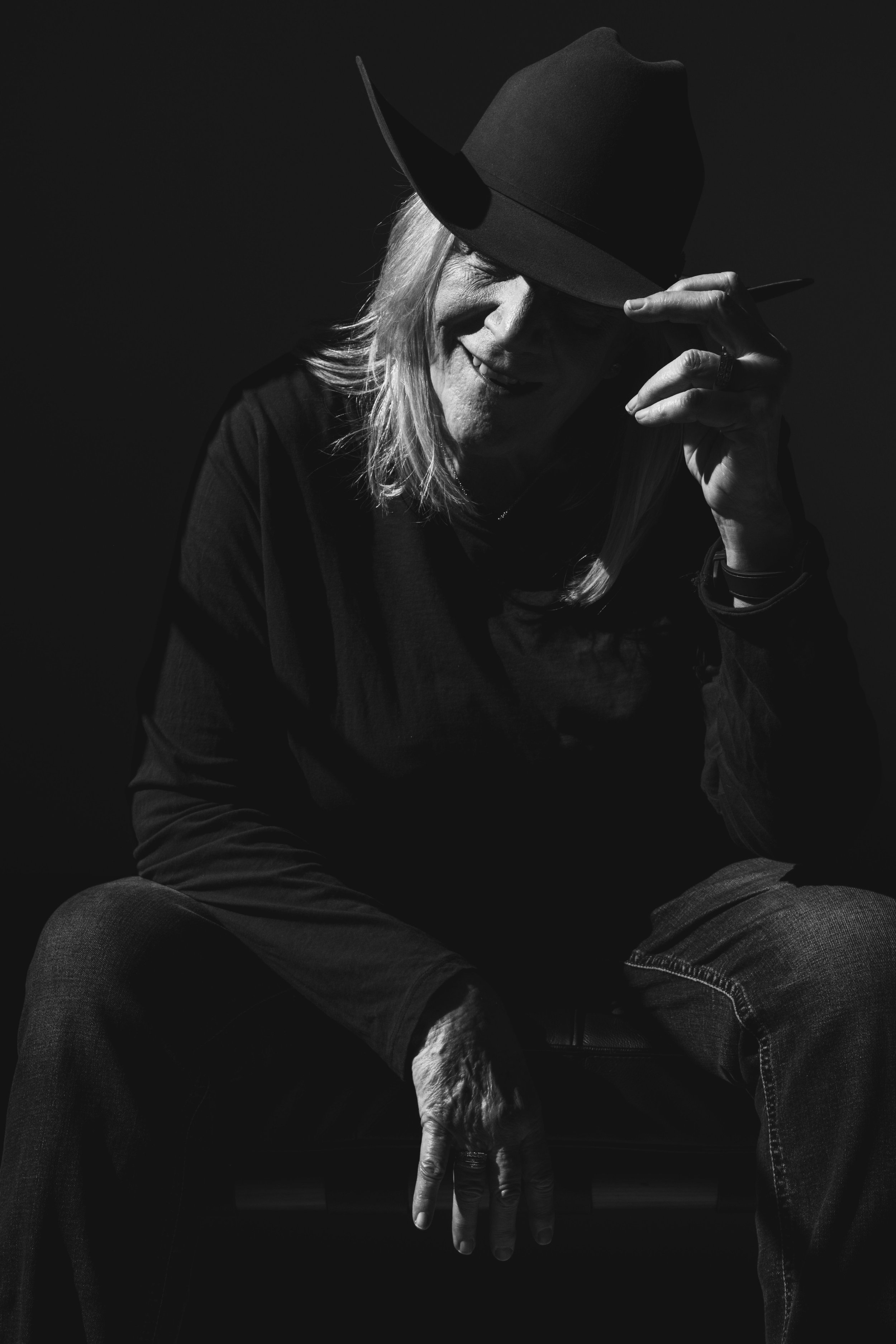 A portrait of a woman who has nothing left to prove. Seated in shadow, hat pulled low, her posture is grounded and intentional. There is strength in her stillness, authority in her restraint. This is confidence that comes from lived experience not pe