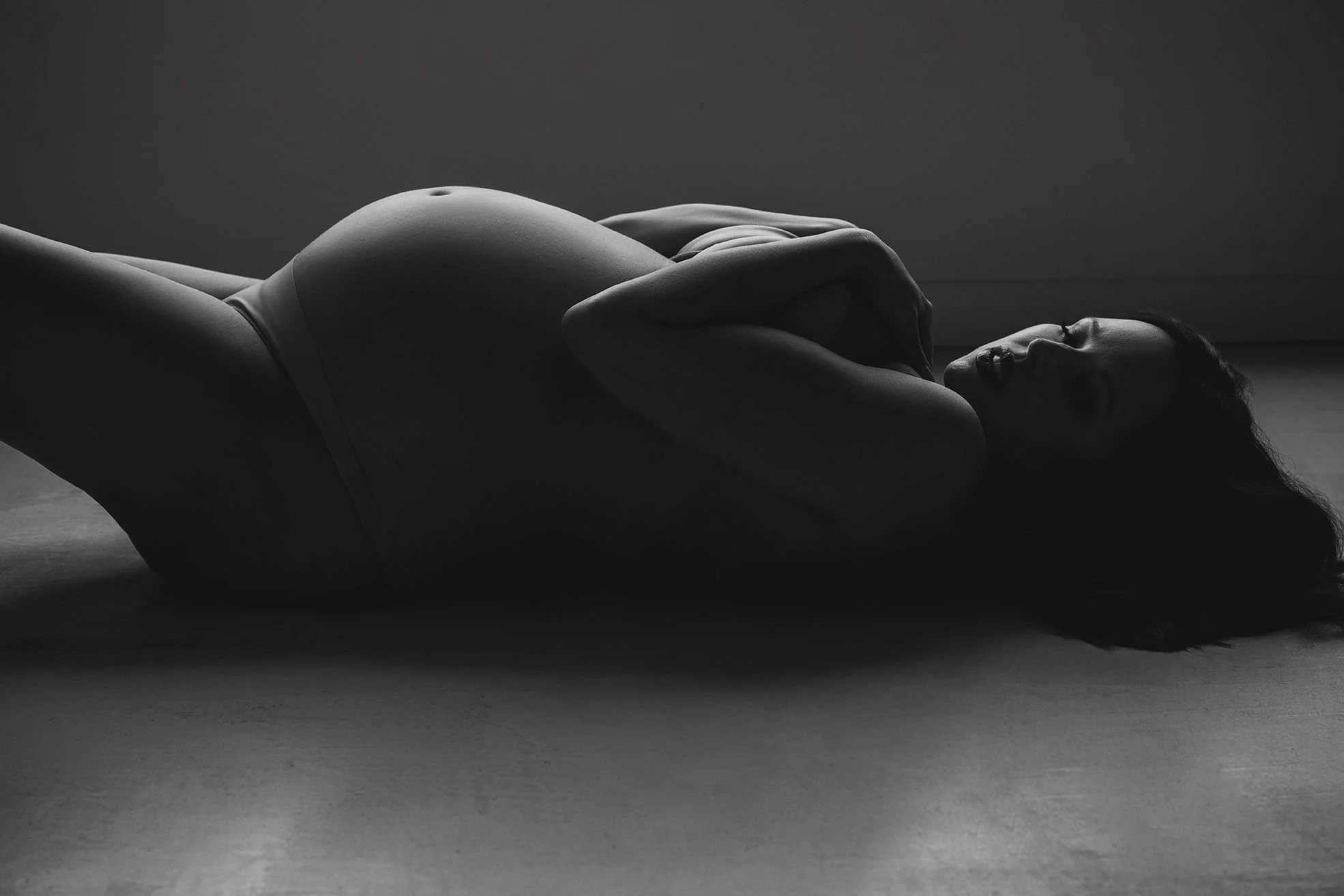 Black and white studio portrait of a pregnant woman lying on her back