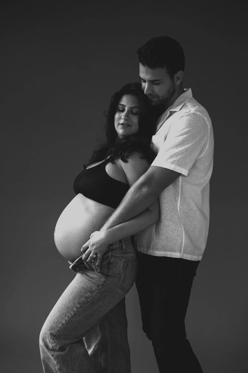 A timeless black and white maternity portrait of an expectant couple in an intimate studio setting, capturing connection, tenderness, and the quiet power of motherhood in Austin, TX.