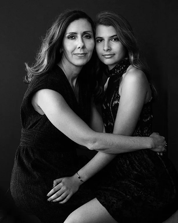 A middle aged beautiful latin woman and her teenage daughter posing closely together in an embrace in a striking, black and white photo