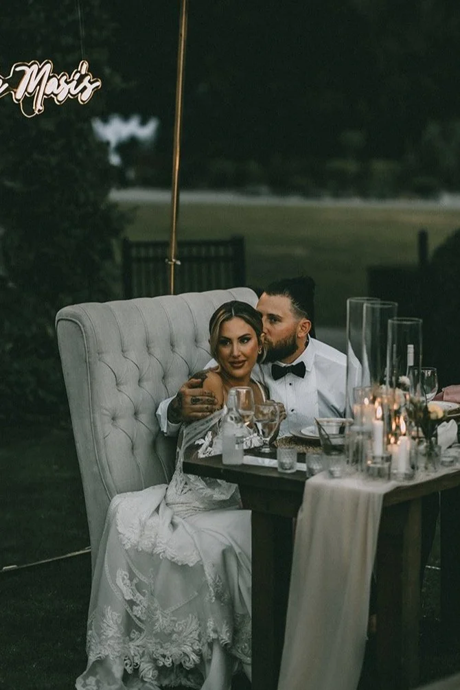 Bride and groom seated at a wedding reception table, embracing, with elegant candlelit decoration.