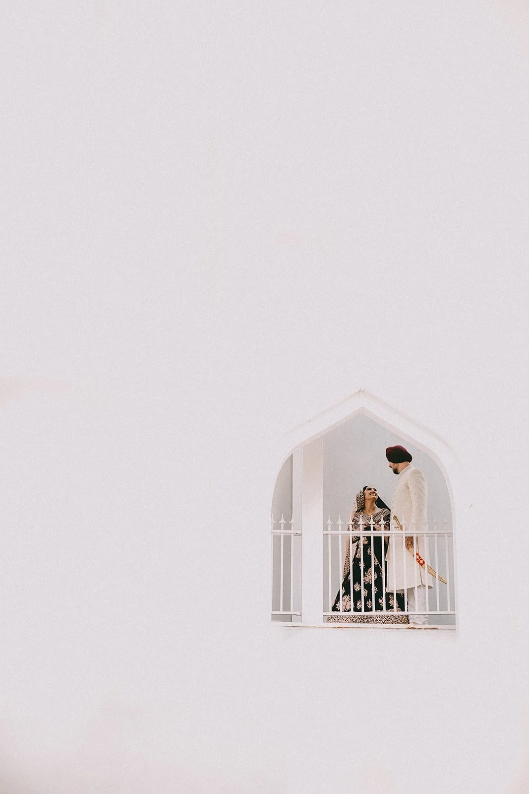 Couple in traditional Indian attire on balcony against white wall