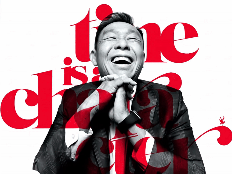 A man in a suit laughing with hands clasped in front of him, with the words "time is a character" in red behind him.