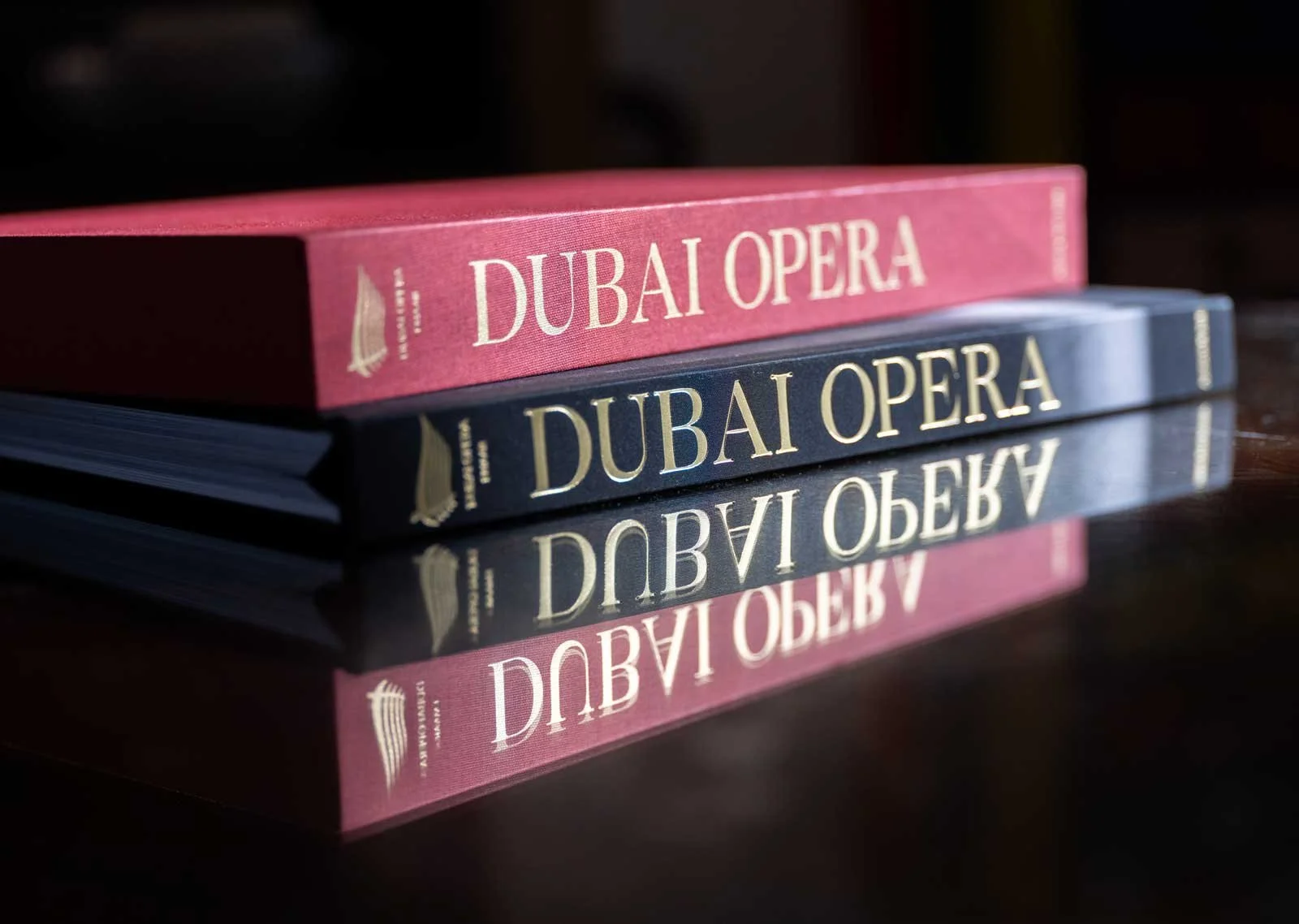 Close-up photograph of Dubai Opera: House of Cultures, published by Assouline, showing the black hardcover book and red presentation case with gold Dubai Opera lettering reflected on a polished surface.
