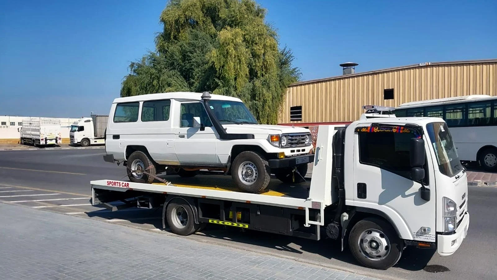 White Toyota Land Cruiser 78 Hardtop with snorkel strapped on a white flatbed recovery truck on an industrial road in the UAE