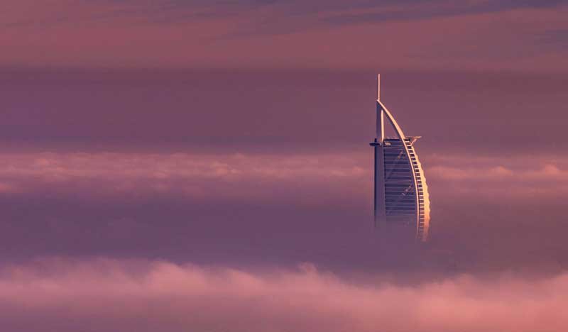 Burj Al Arab rising above morning fog beneath a pink and violet sky in Dubai.
