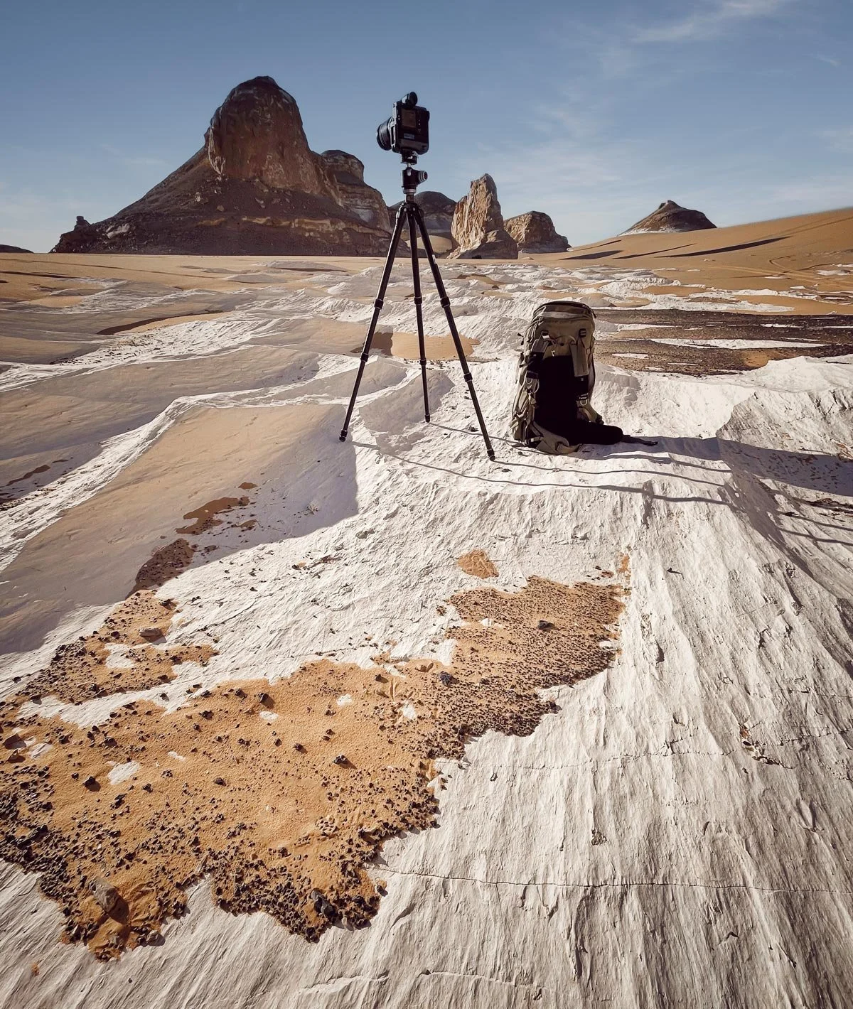 A camera, tripod and backpack set among chalk terrain and towering desert rocks during Dany Eid’s landscape photography journey in Egypt.