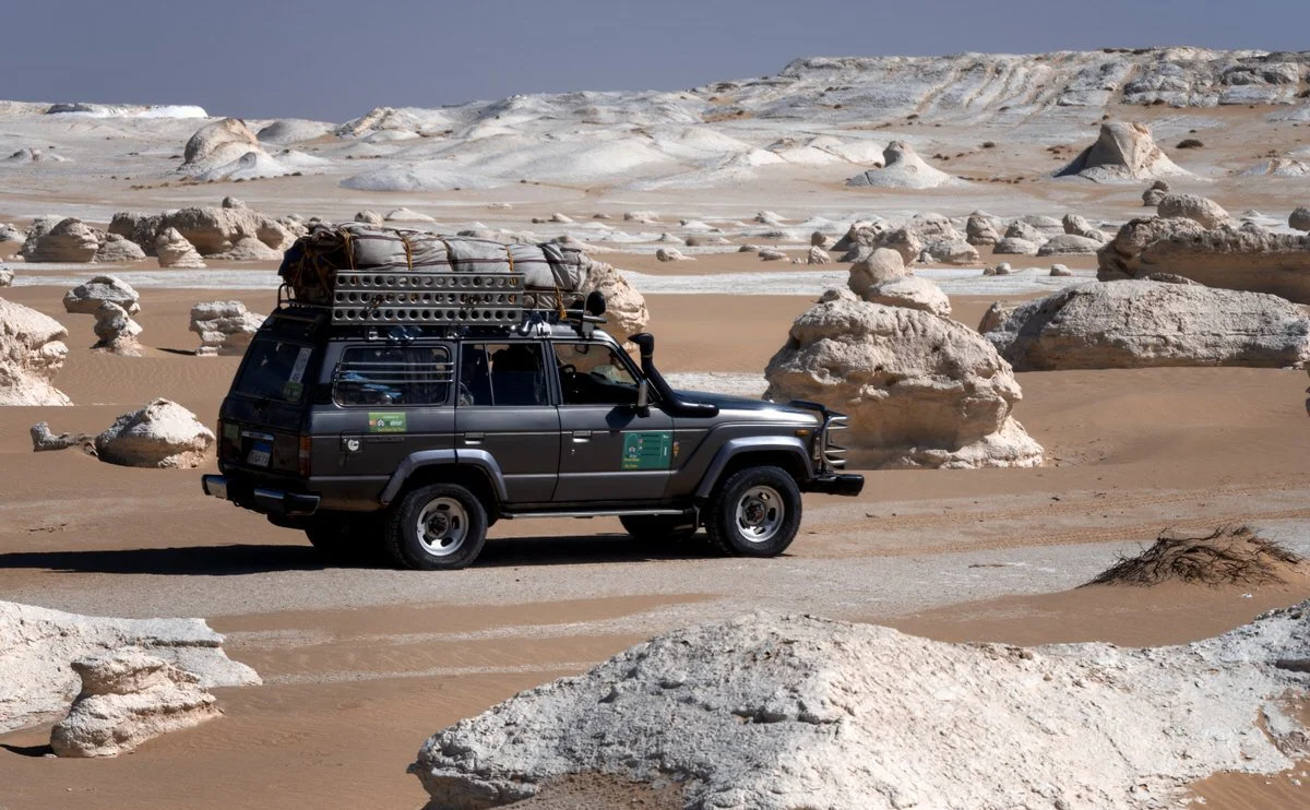 A Toyota Land Cruiser navigates white rocky terrain beneath towering desert walls in Egypt, photographed by Dany Eid during an overland journey.