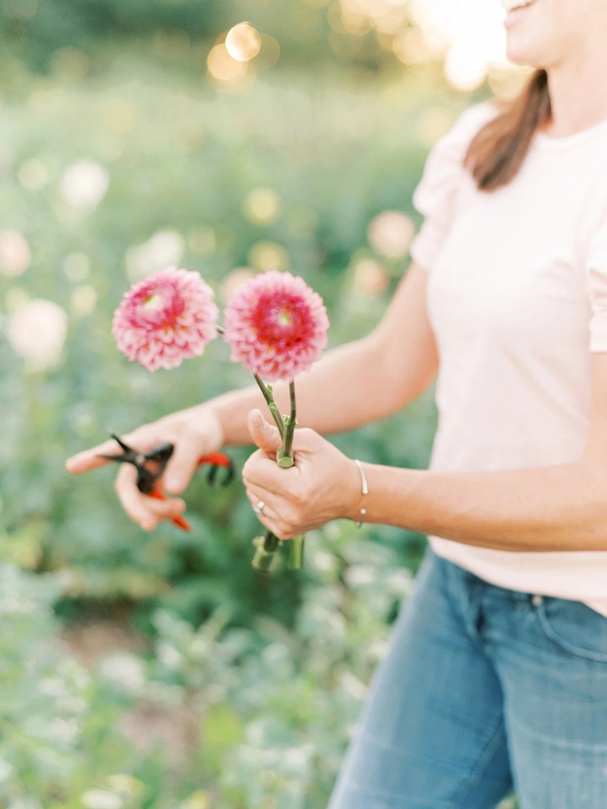 Jenn from PepperHarrow, holding two dahlia blooms that she just cut out of the dahlia field.