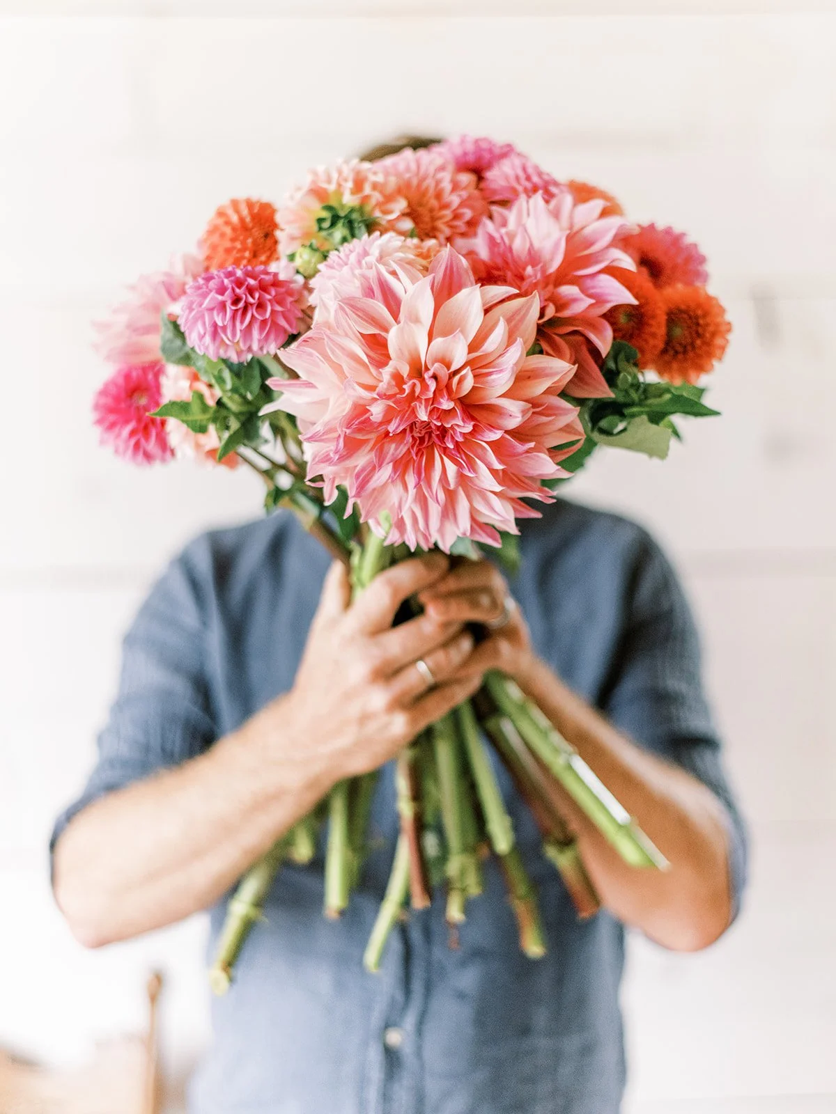 A flower farmer holding a large bouquet of dahlias in front of his face