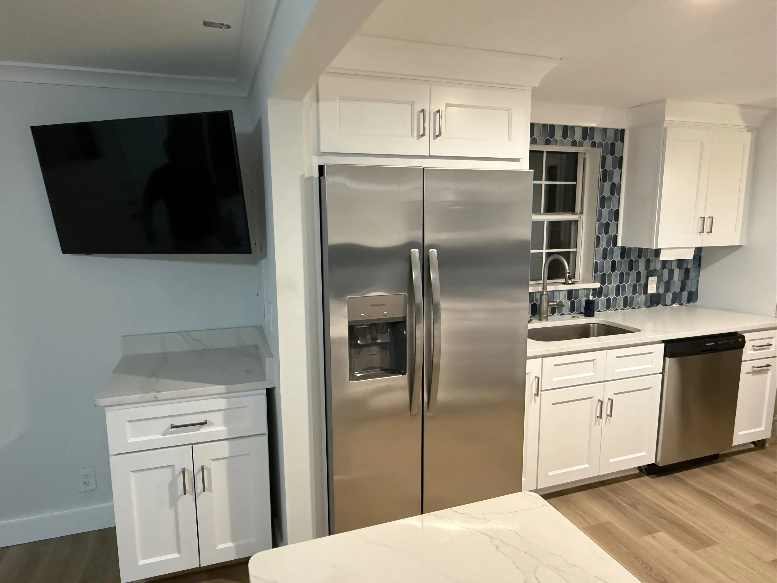 A remodeled kitchen with white shaker cabinets, quartz countertops, stainless steel appliances, and a blue hexagonal tile backsplash.