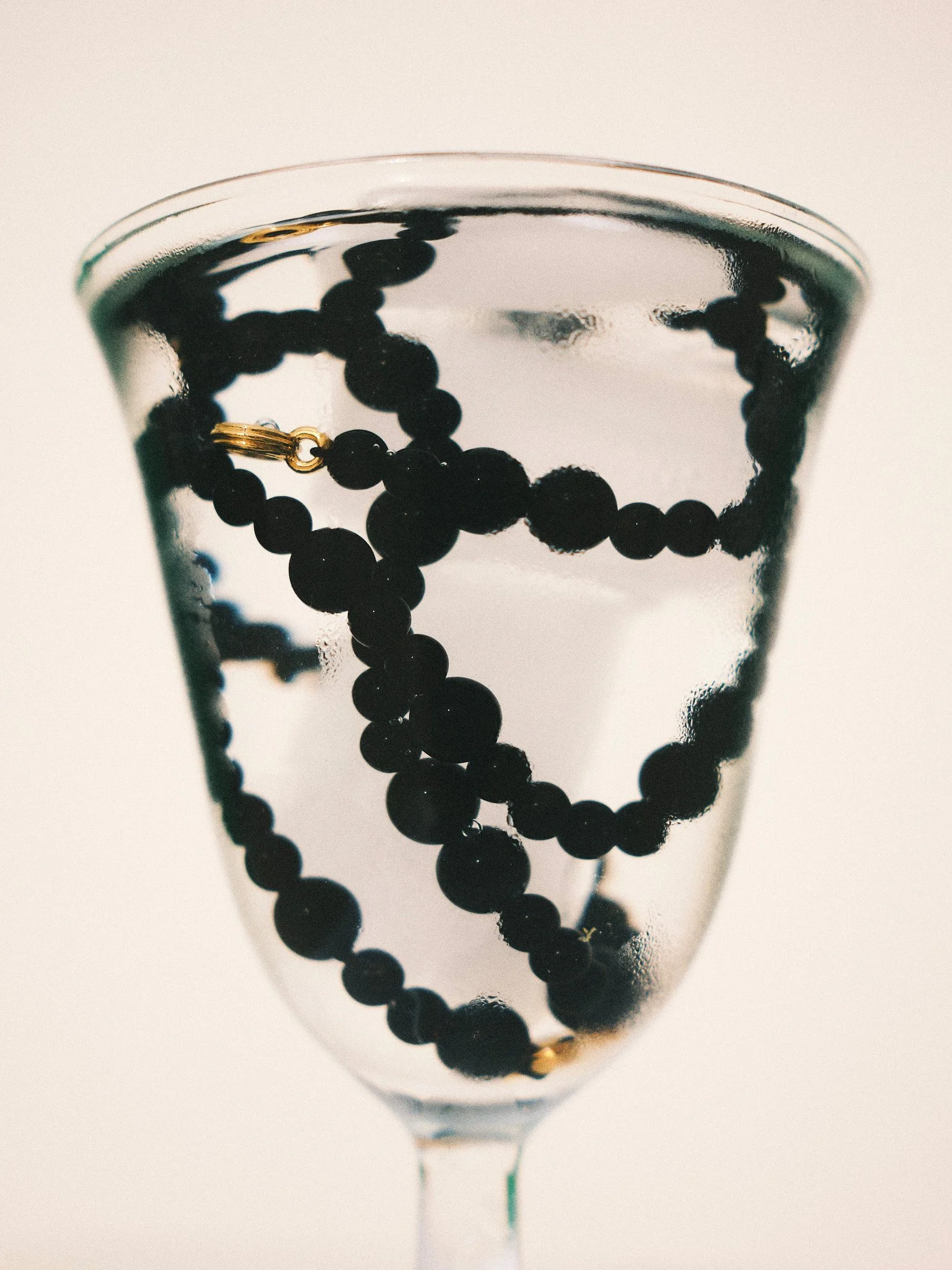 Editorial jewelry still life of a black beaded necklace inside a clear glass photographed in soft natural light.