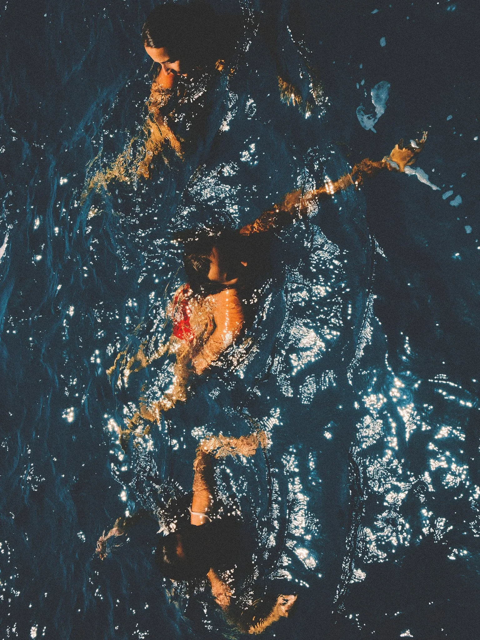 Swimmers in the deep blue Mediterranean Sea in Menorca, photographed from above in shimmering summer sunlight