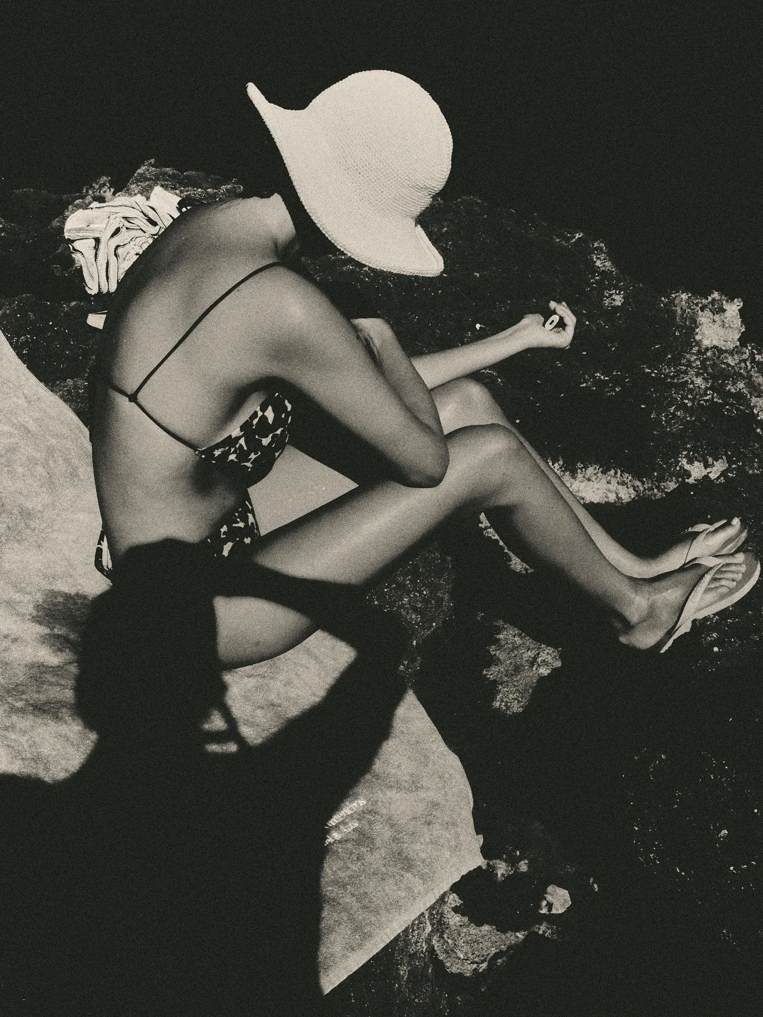 `Black and white editorial travel photograph of a woman sunbathing on the rocky Mediterranean coast of Menorca in summer