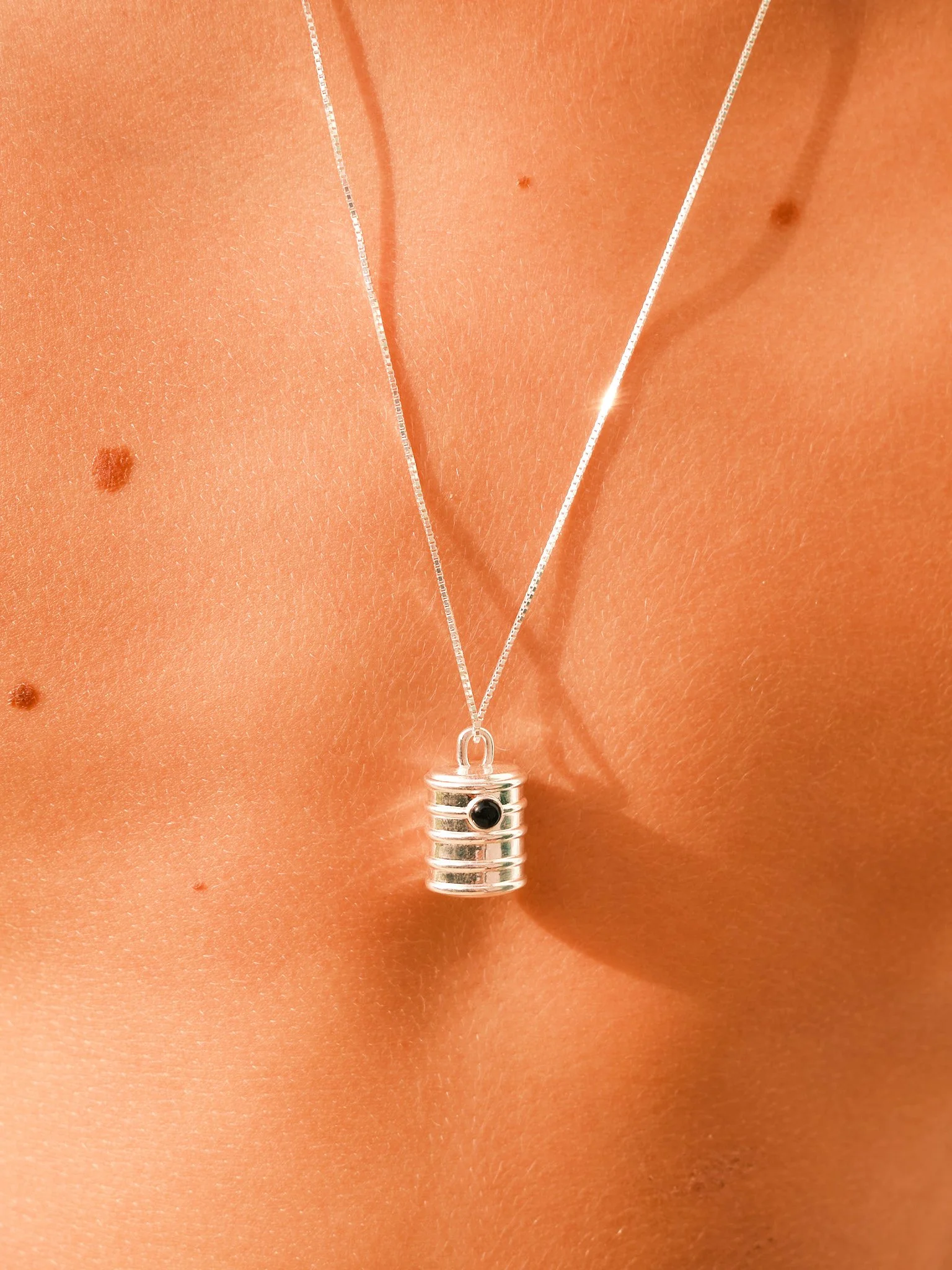 `Editorial jewelry close-up of a silver pendant necklace on sun-kissed skin, photographed in bright natural summer light.