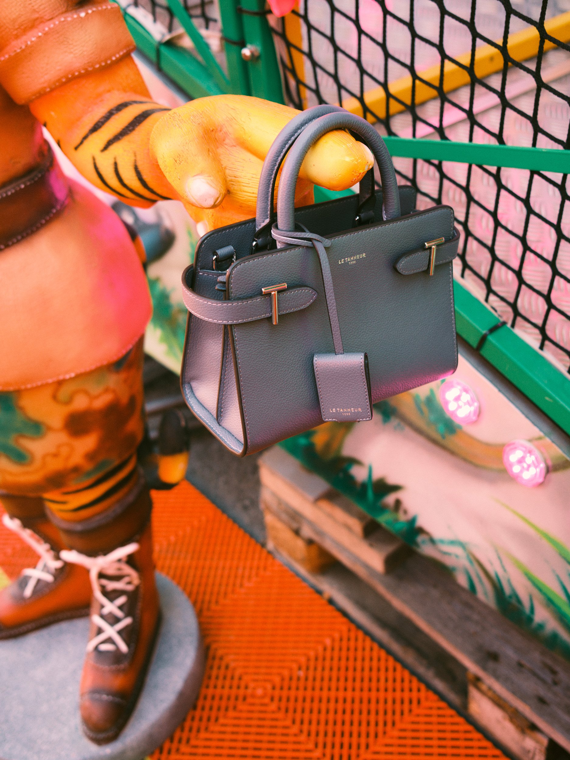 Editorial fashion still life of a black Le Tanneur leather handbag displayed in a colorful fairground ride, photographed with playful saturated tones.