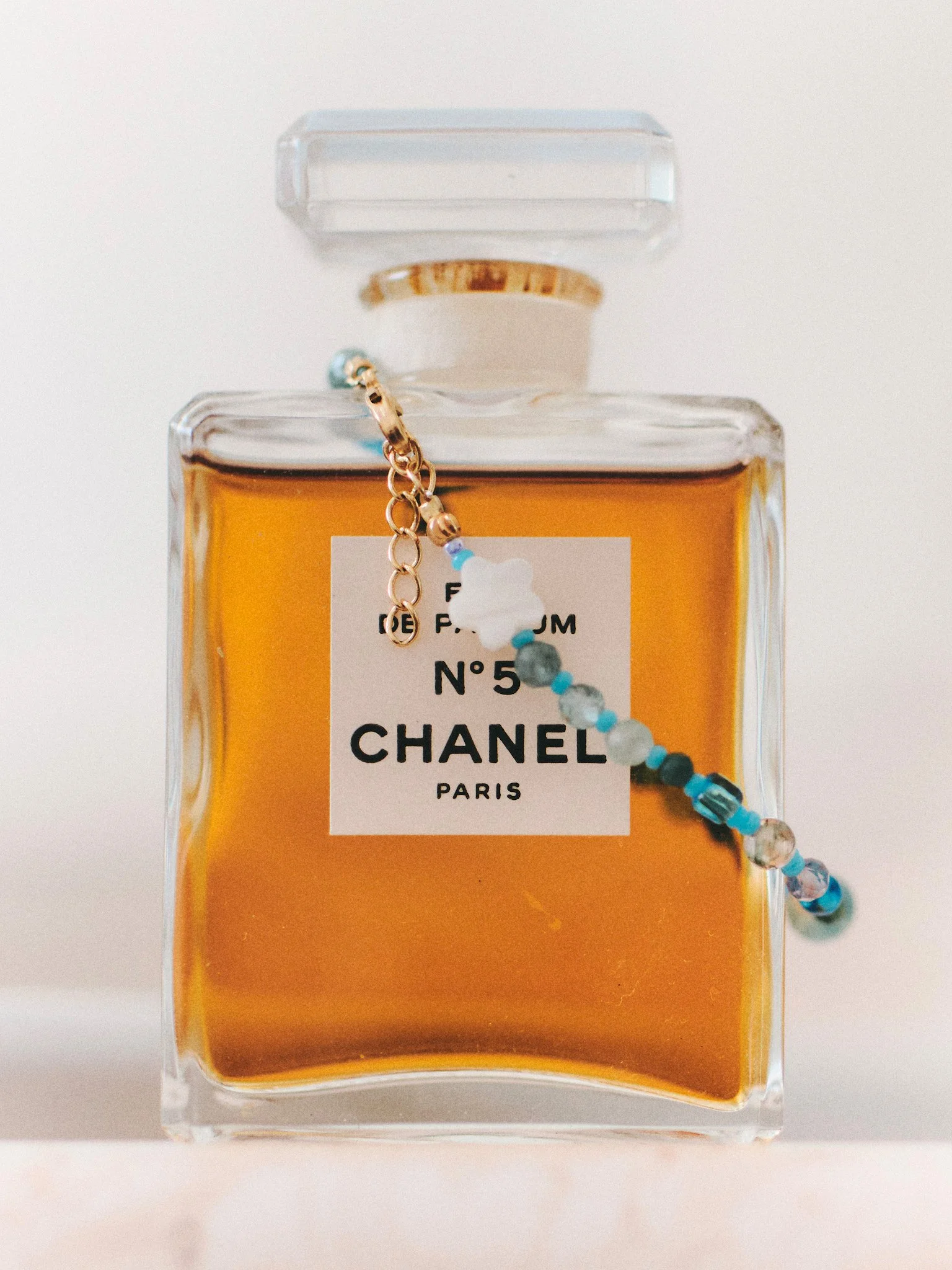 Editorial still life of blue beaded jewelry draped over a Chanel No. 5 perfume bottle, photographed in soft natural light.