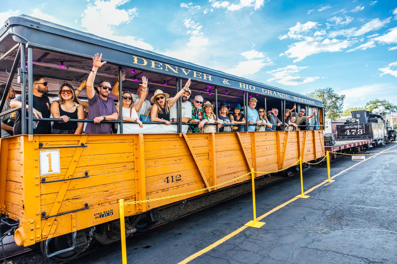 Passengers smile and wave from the open-air gondola car aboard the Durango Blues Train.