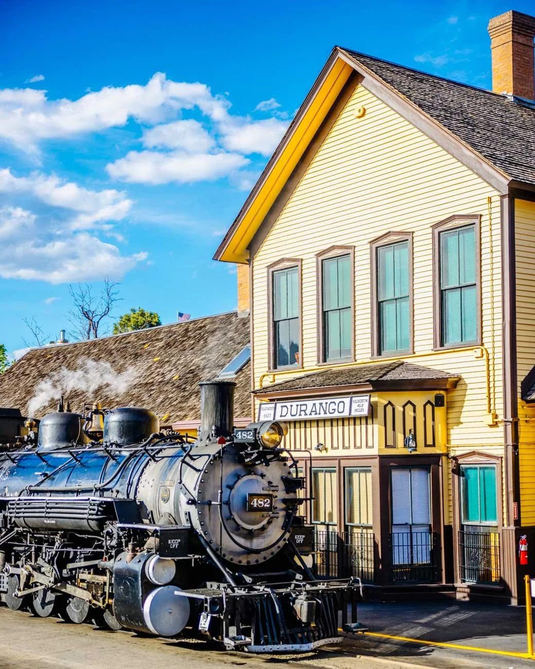 The Durango Blues Train sits in front of the historic Durango & Silverton Narrow Gauge Railroad Depot before departure, with passengers gathering to board for an evening of live blues music and scenic mountain views.