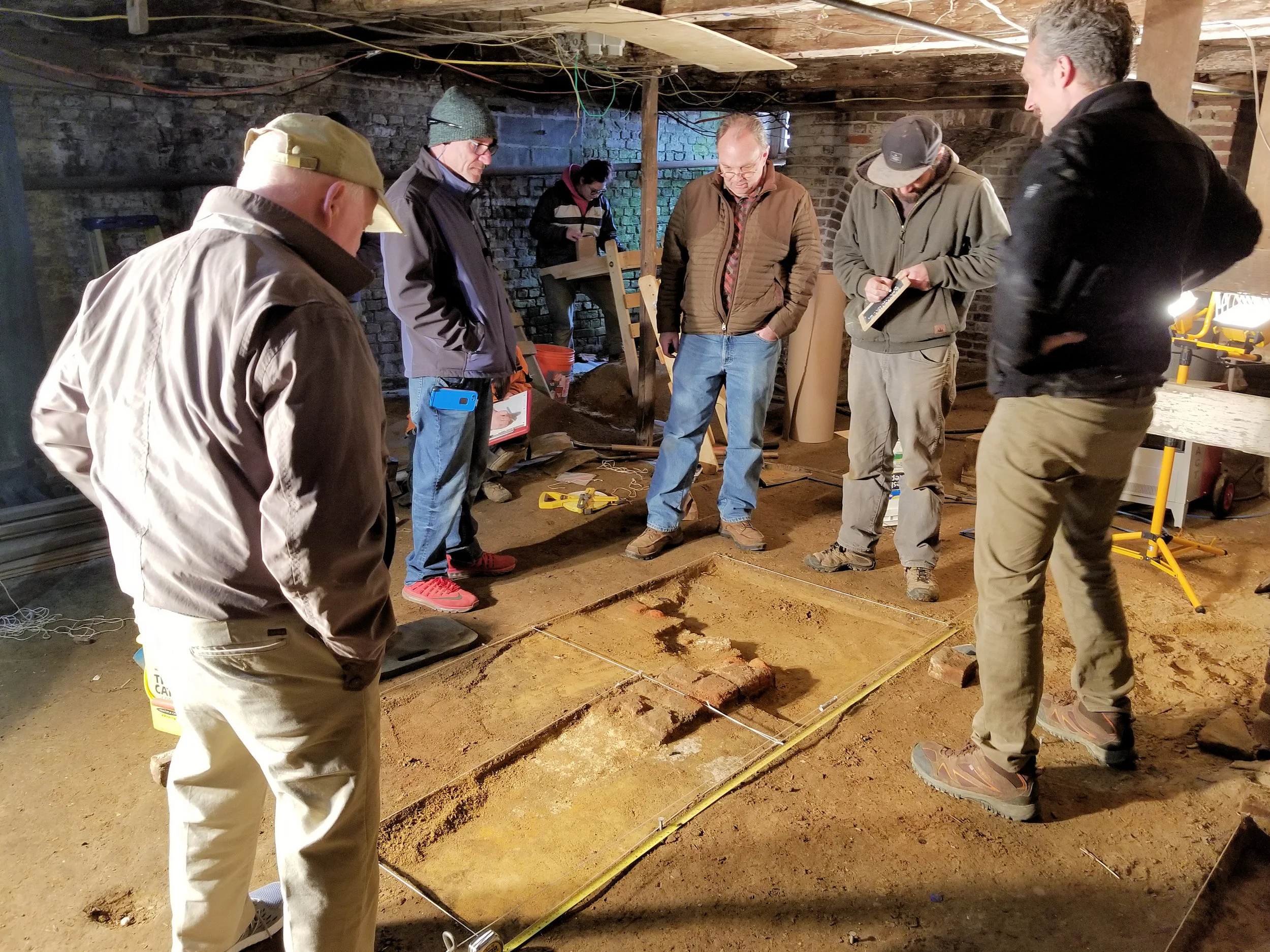 the team examining a discovered foundation in the basement
