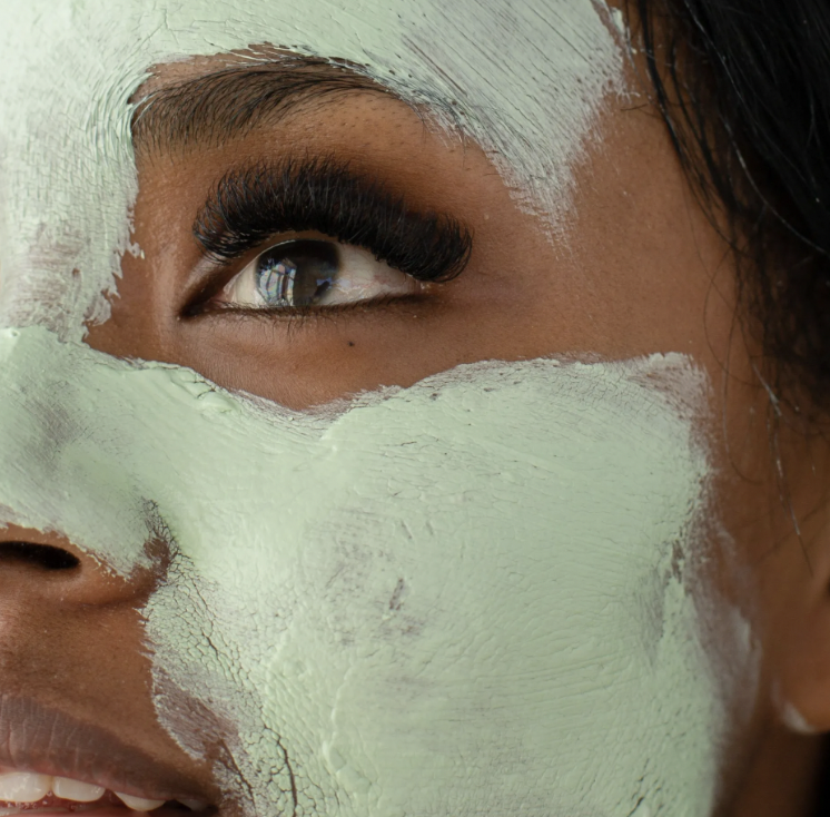 Close-up of a person with dark skin, partially covered in light green paint around the eye, nose, and cheek area.