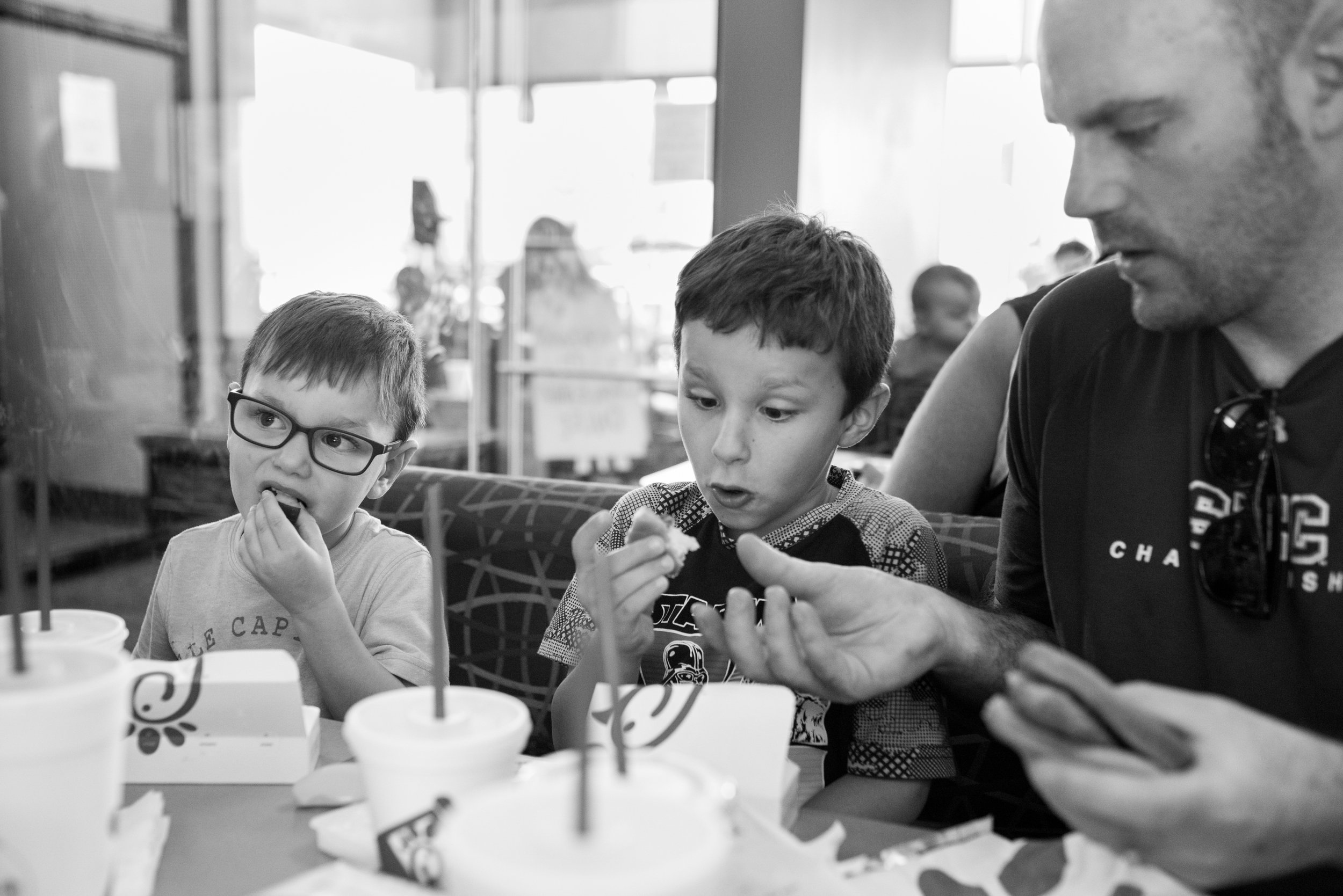 Dad handing son food at table at Chick-Fil-A while other son is eating