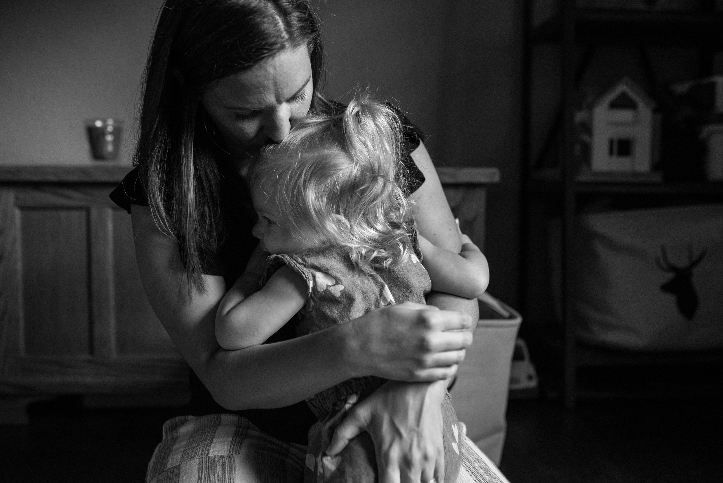 Mom hugging toddler daughter and kissing her on the forehead