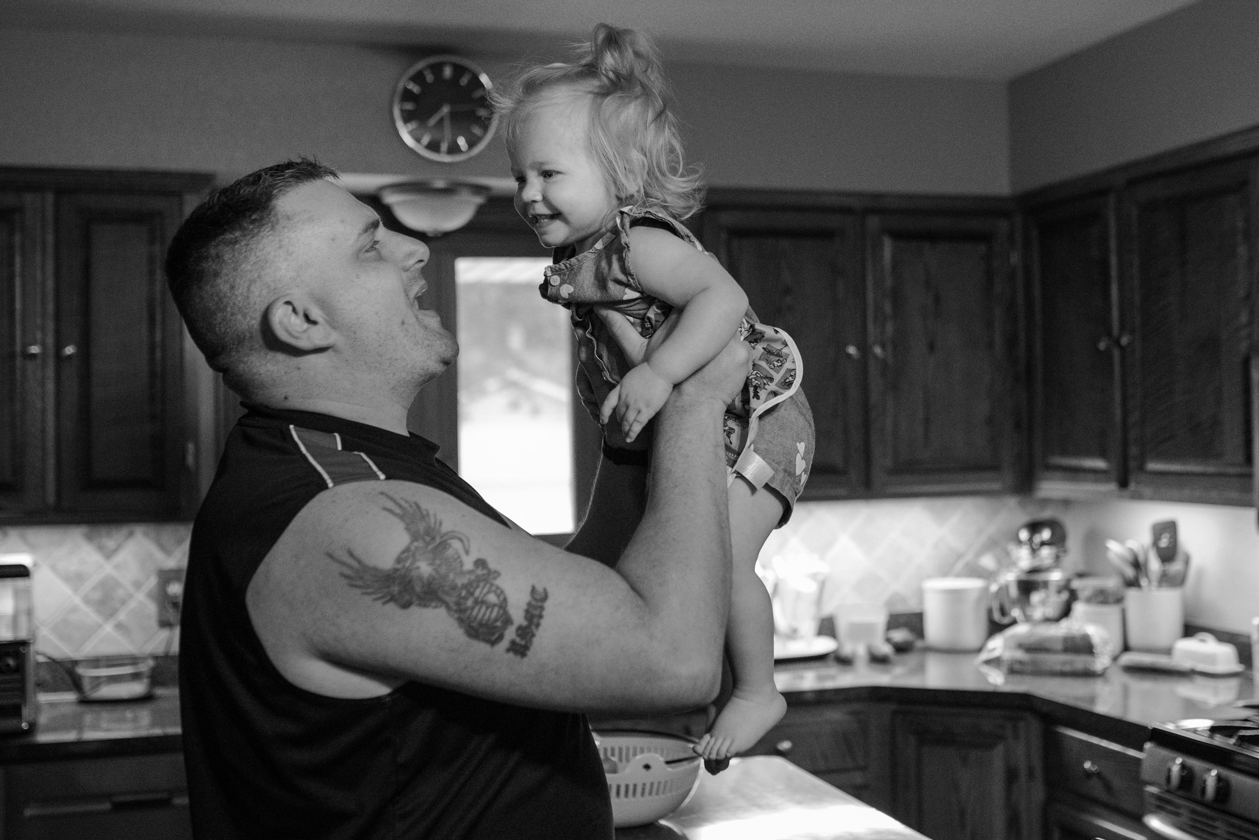 Dad holding up smiling toddler daughter in the kitchen