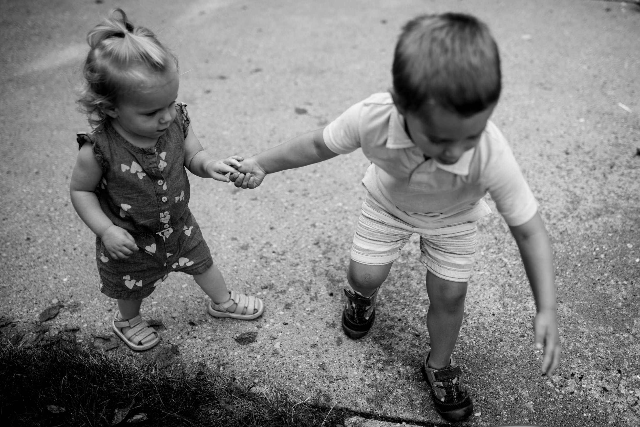 Brother holding sisters hand and leading her on the driveway during a West Bend family in home session