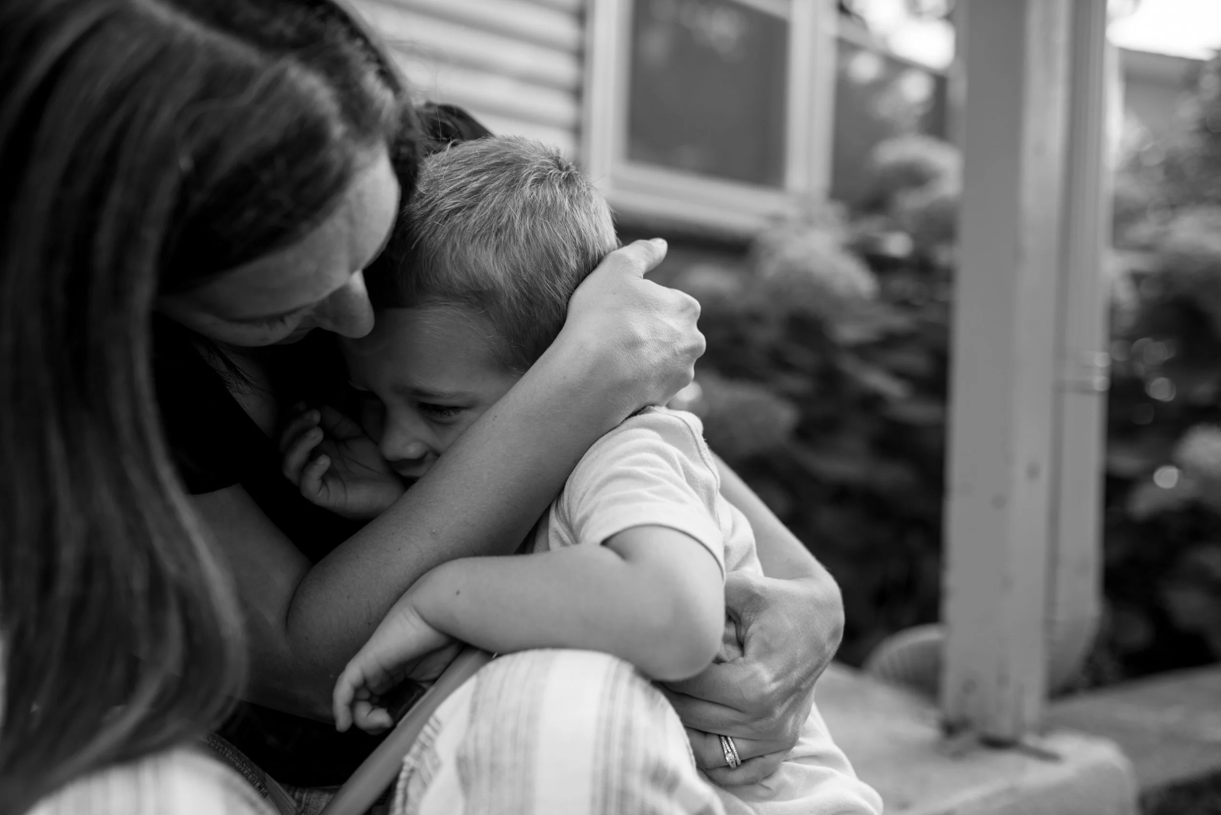 Mom holding toddler son in her arms sitting on the porch