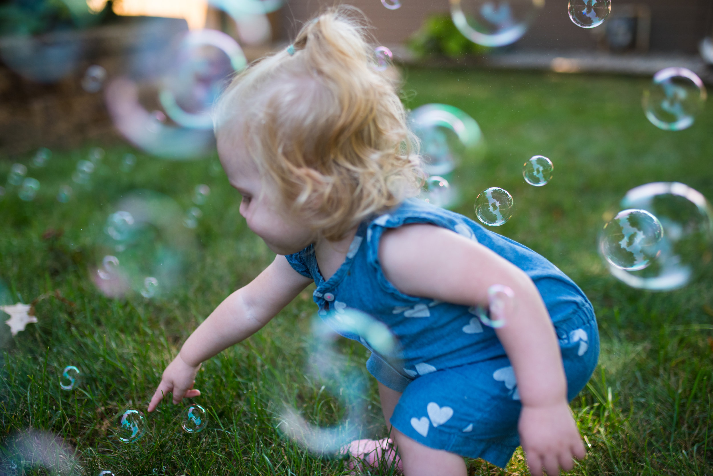 Toddler girl trying to poke bubbles in the grass